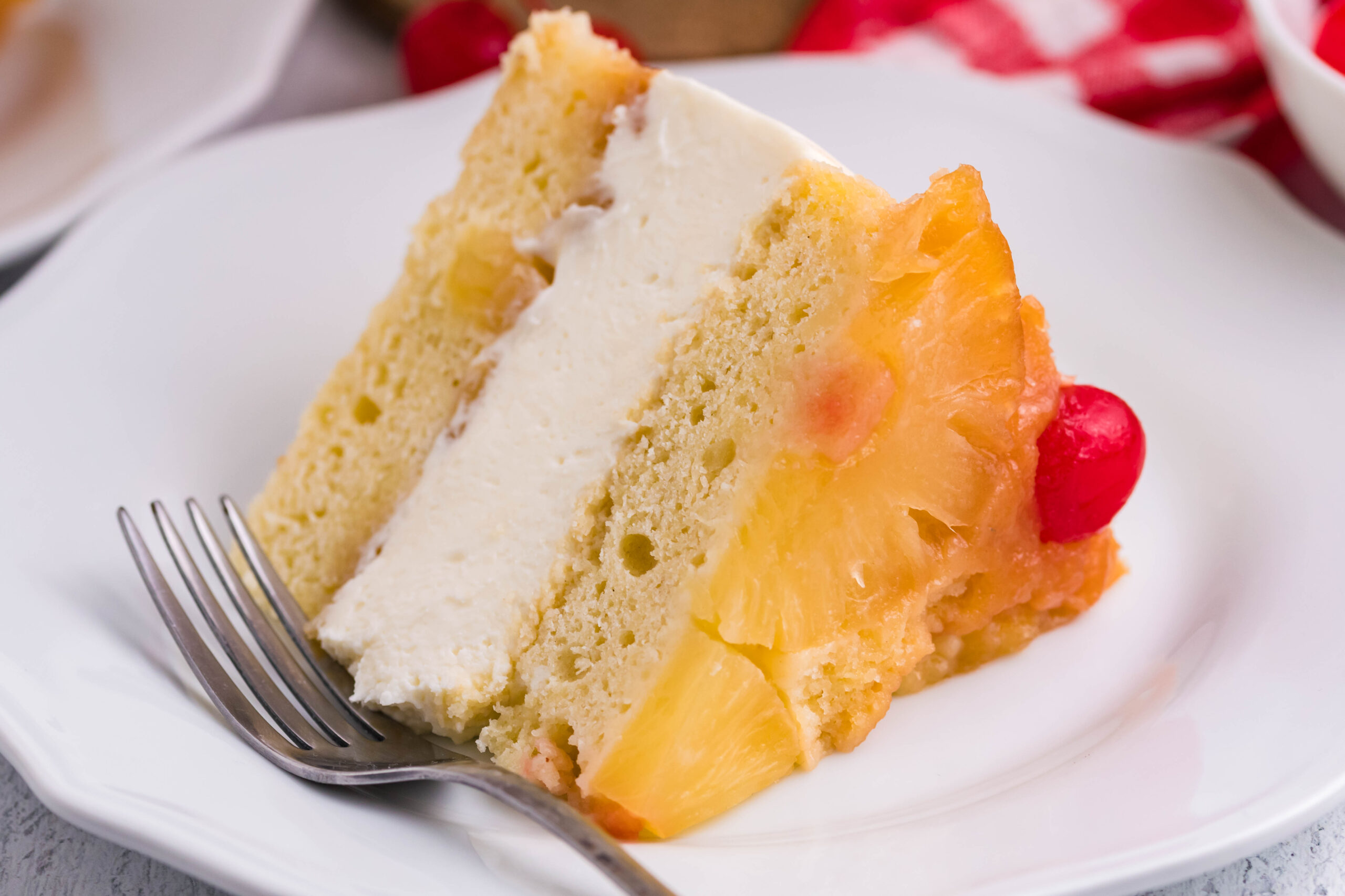 Front view of a slice of Pineapple Upside Down Cheesecake Cake served on a white plate with a silver fork.