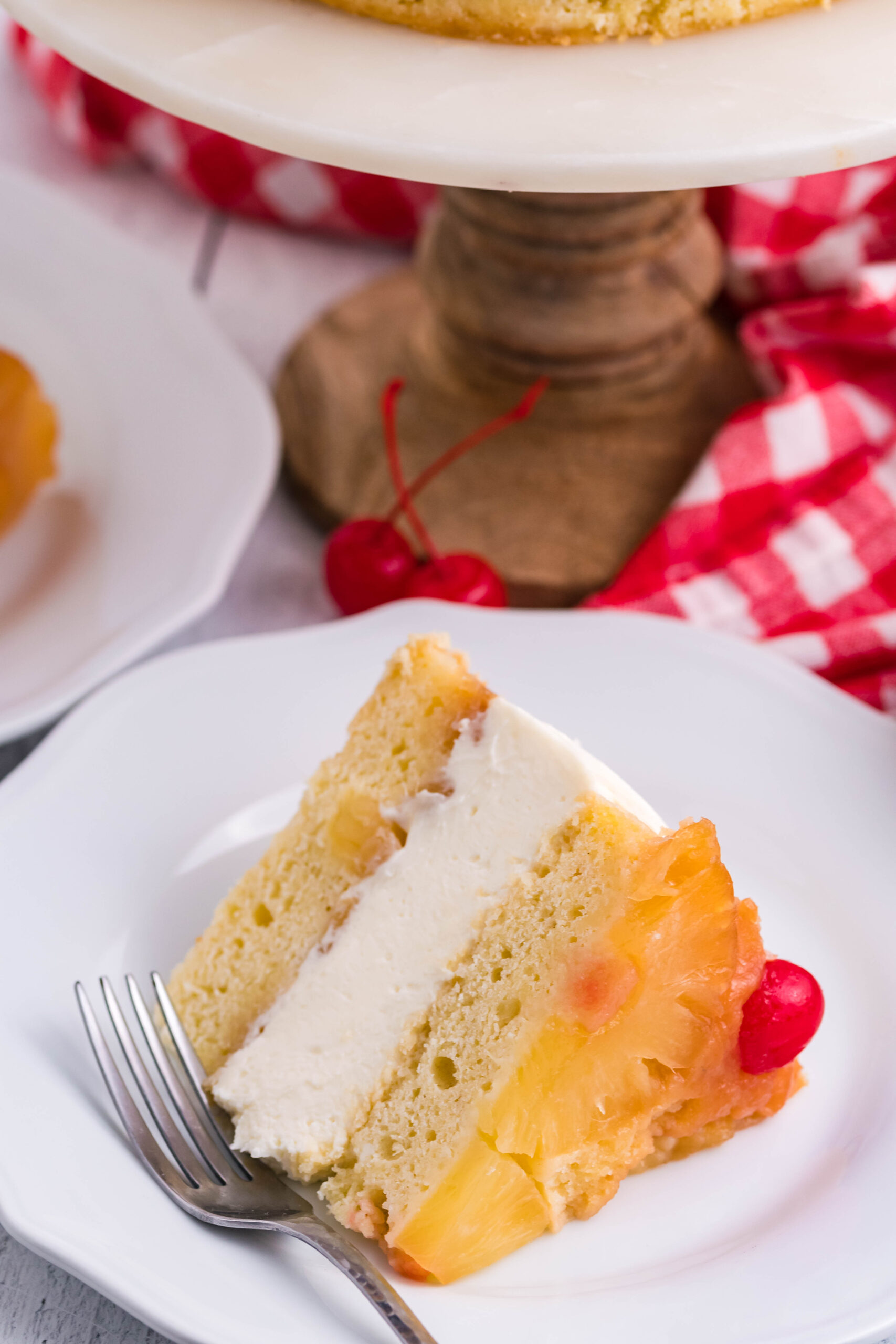 Front view of a slice of Pineapple Upside Down Cheesecake Cake served on a white plate with a silver fork.