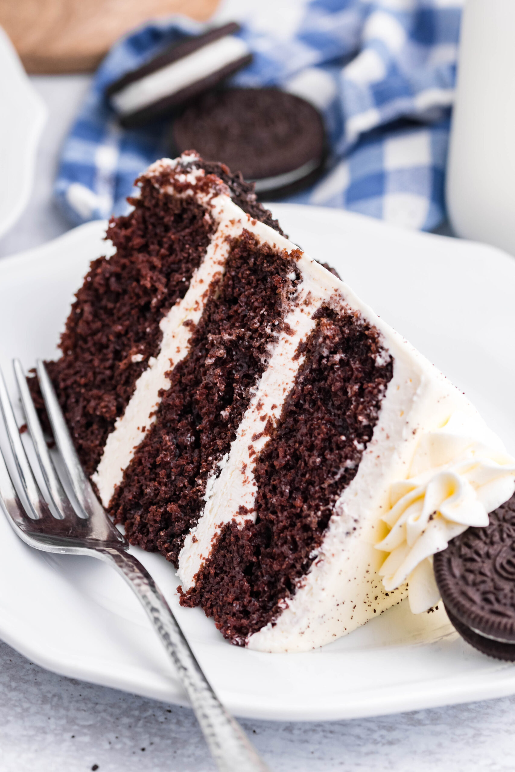 Front view of a slice of Double Stuffed Oreo Cake served on a white plate with a silver fork.