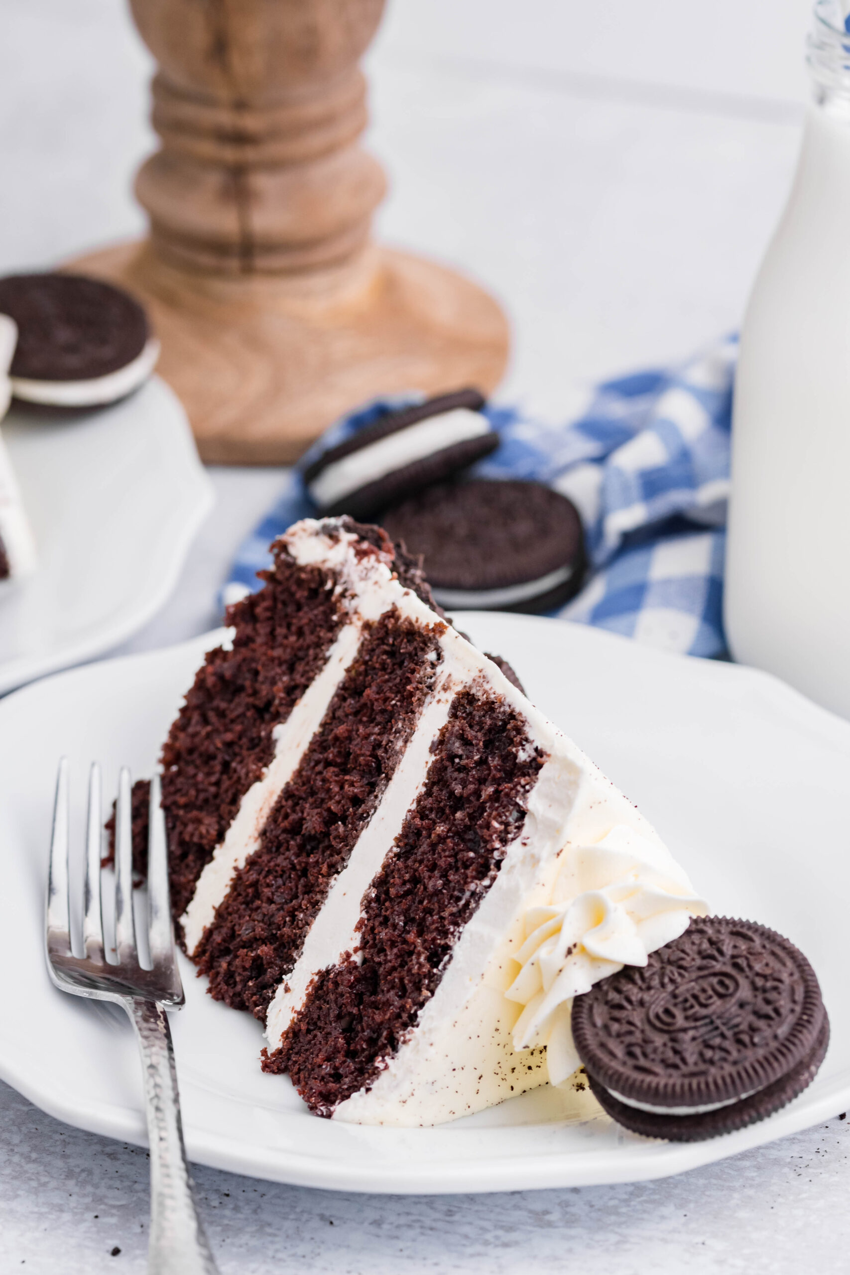 Front view of a slice of Double Stuffed Oreo Cake served on a white plate with a silver fork.