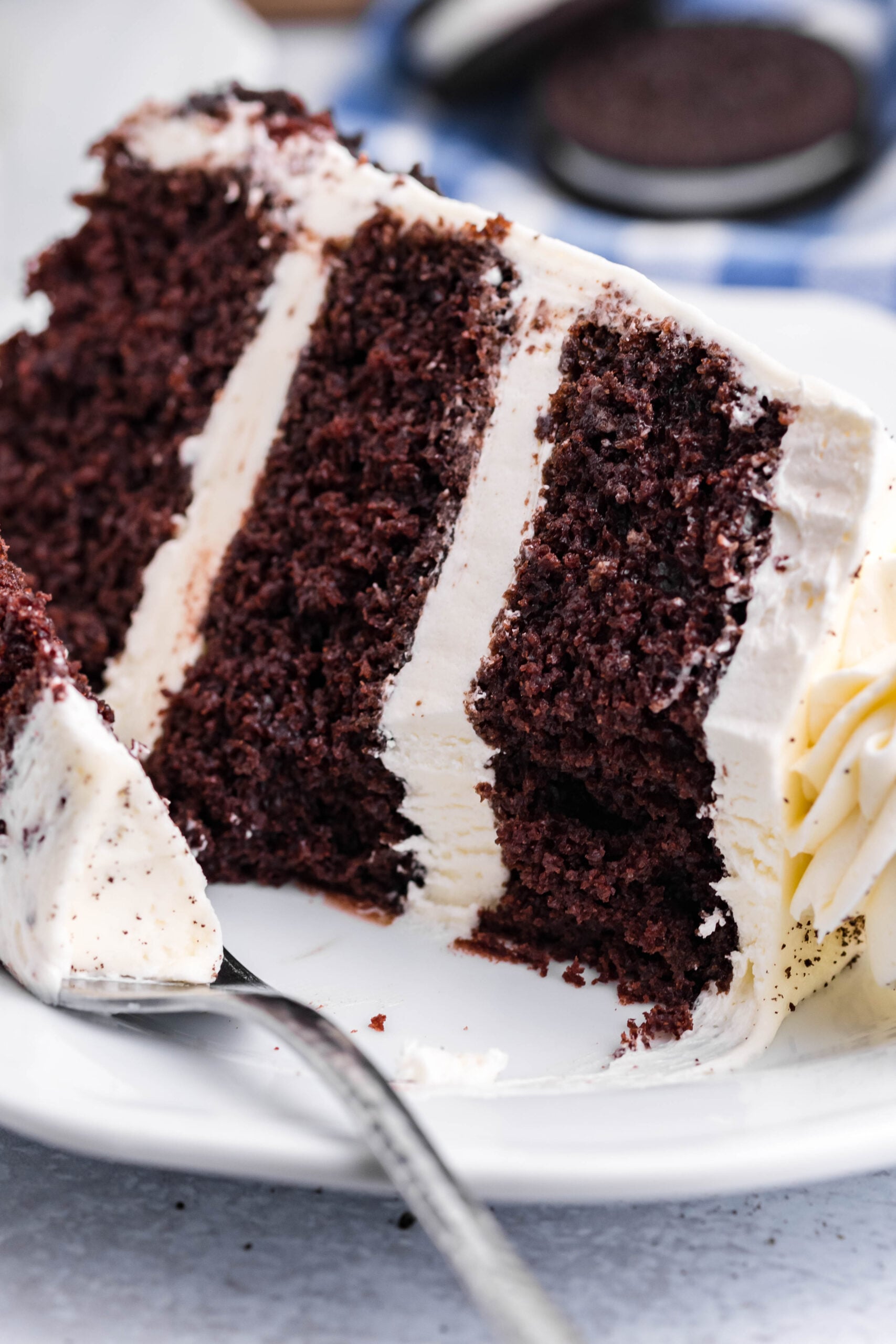 Close up view of a slice of Double Stuffed Oreo Cake served on a white plate with a bite removed from a silver fork.