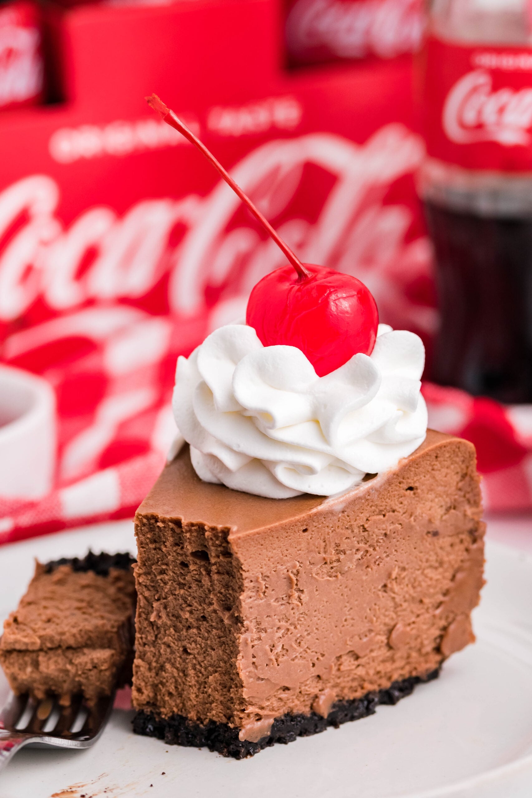 Side view of a slice of Coca Cola on a white dish with a piece removed and on a fork.