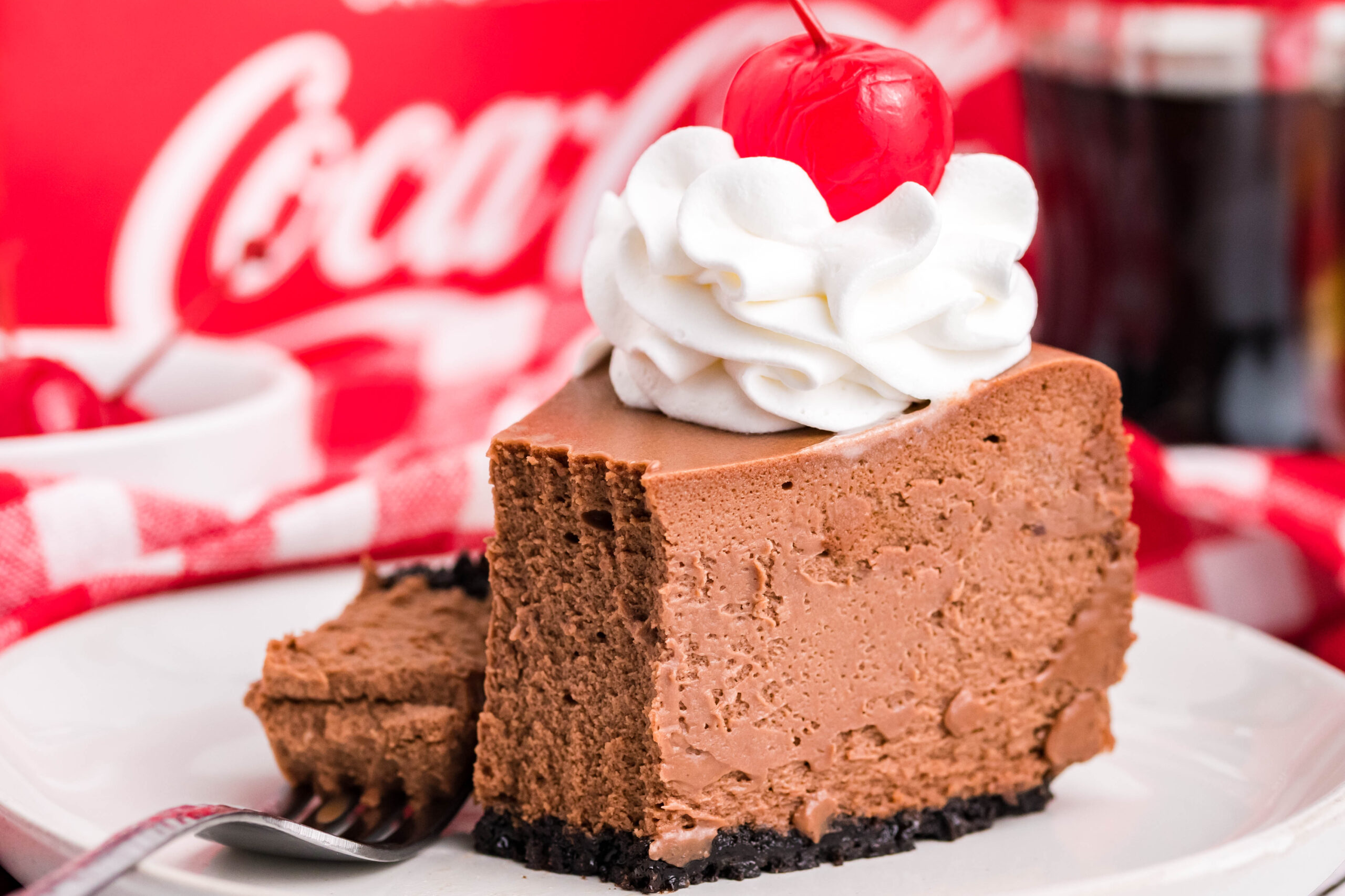 Side view of a slice of Coca Cola on a white dish with a piece removed and on a fork.