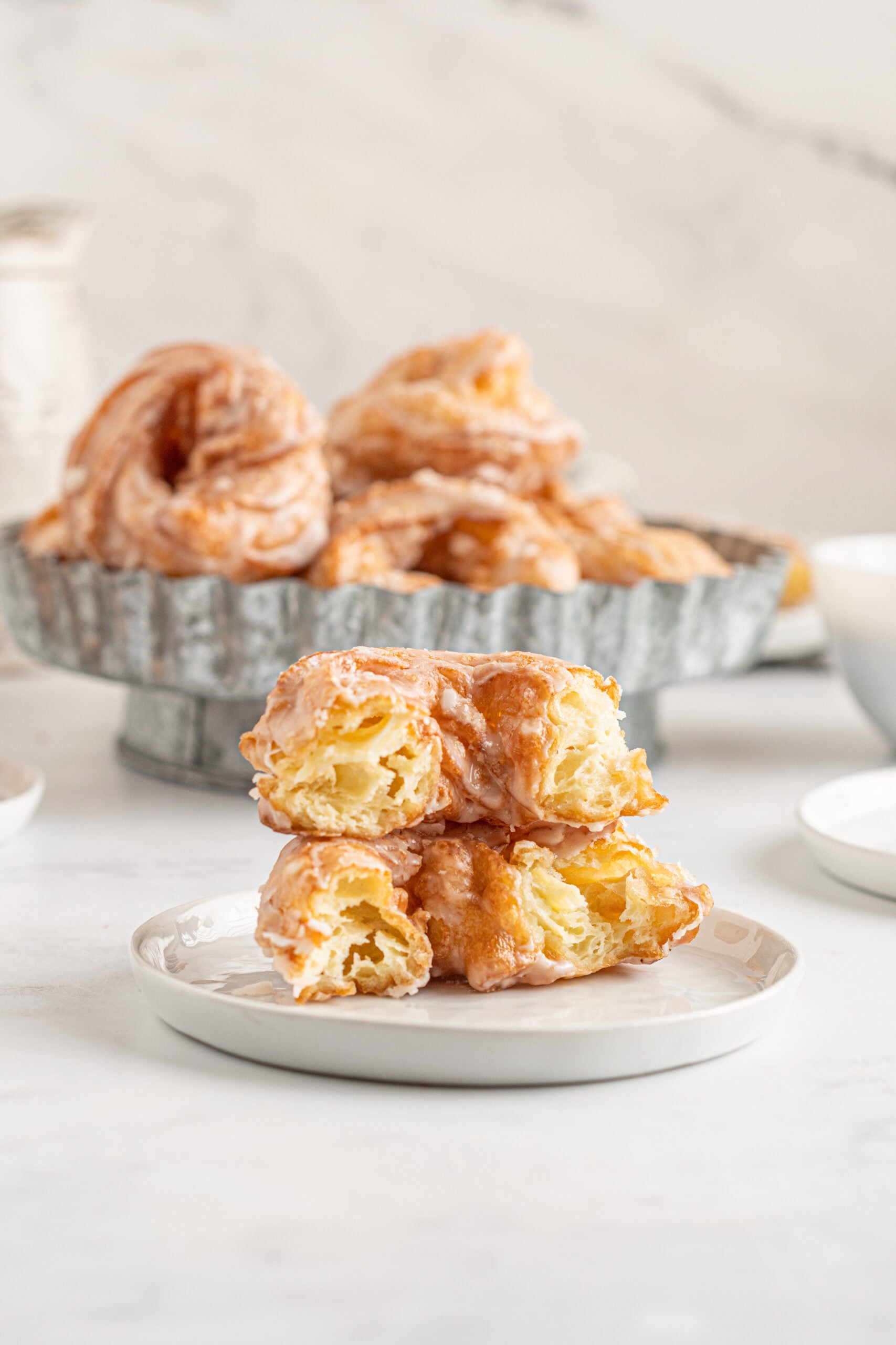 Front view of 2 half French Crullers stacked on a white dish. 