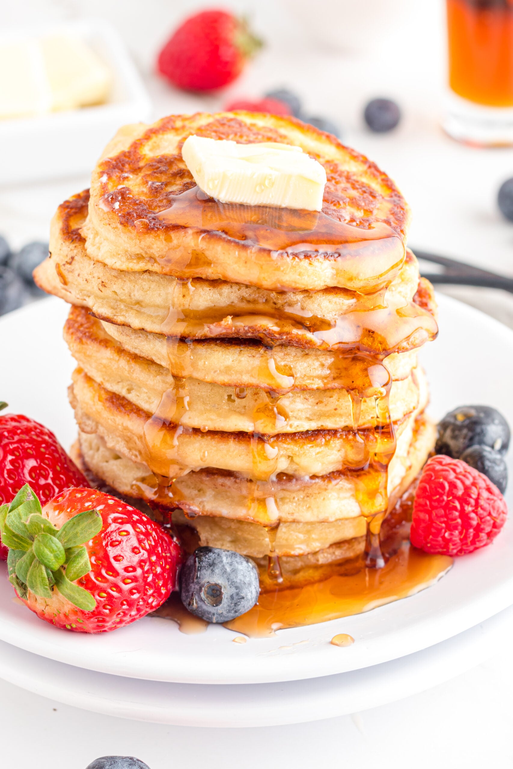 Close up shot of Mini Pancakes stacked on a white plate topped with syrup and butter