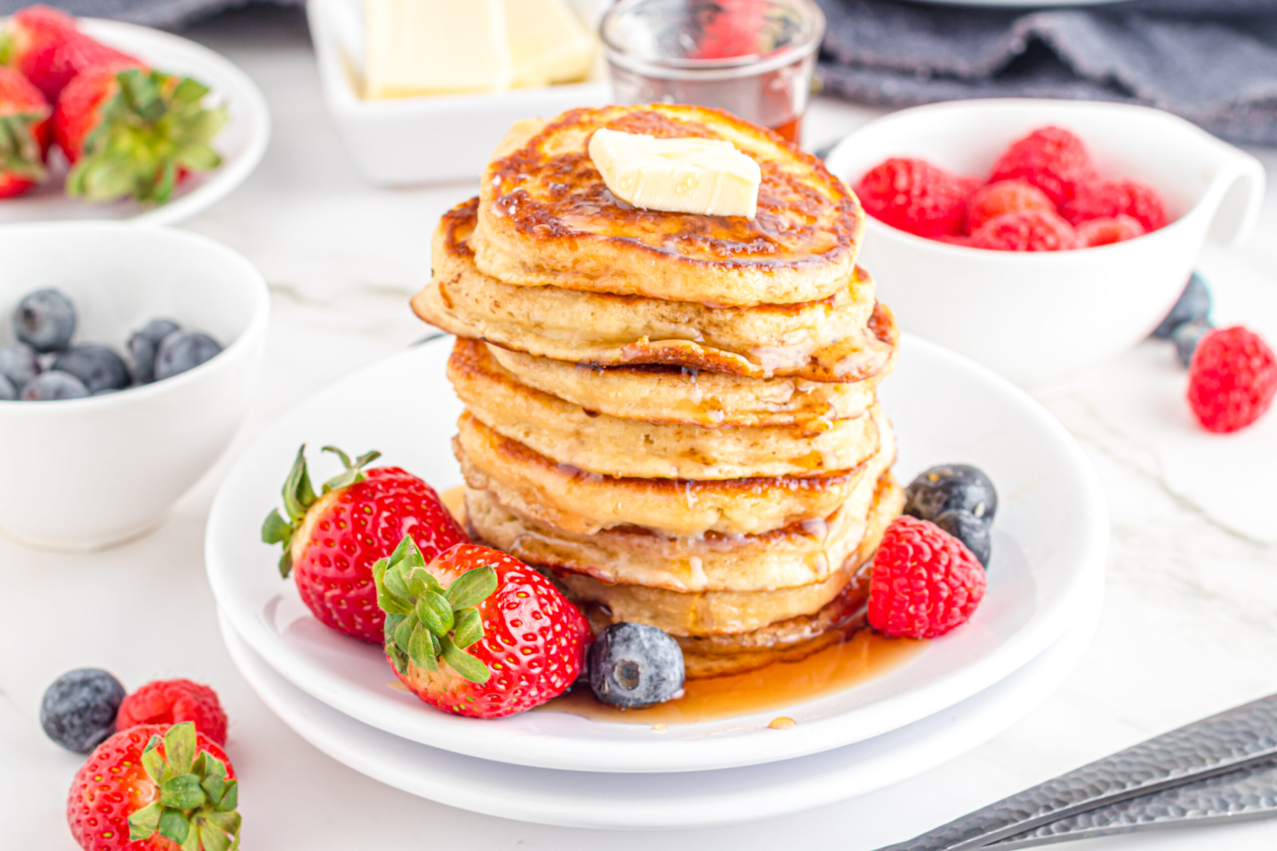 Mini Pancakes stacked on a white plate topped with syrup and butter