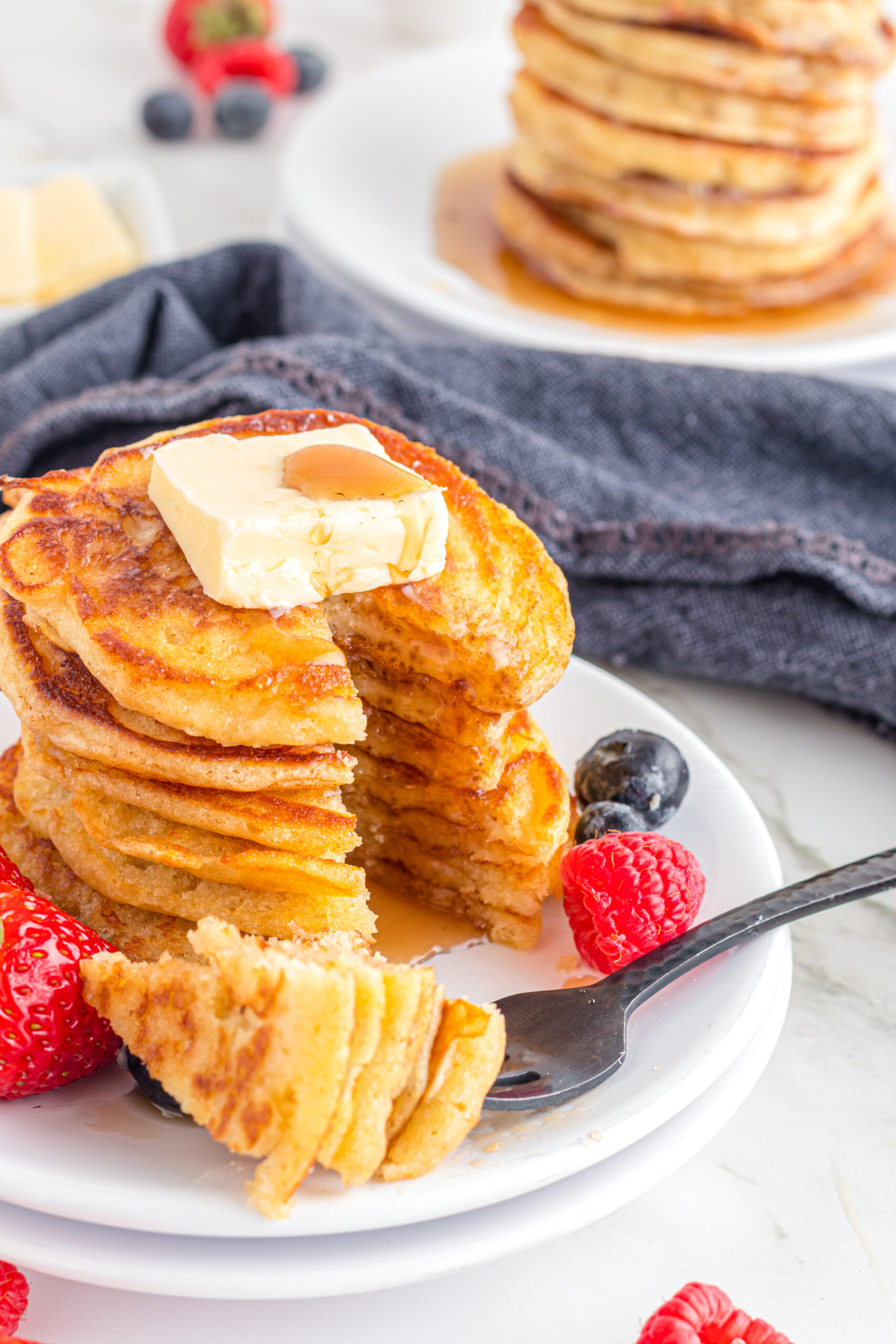 Front view of Mini Pancakes on a white dish served with strawberries and blueberries with a bite removed from a silver fork.