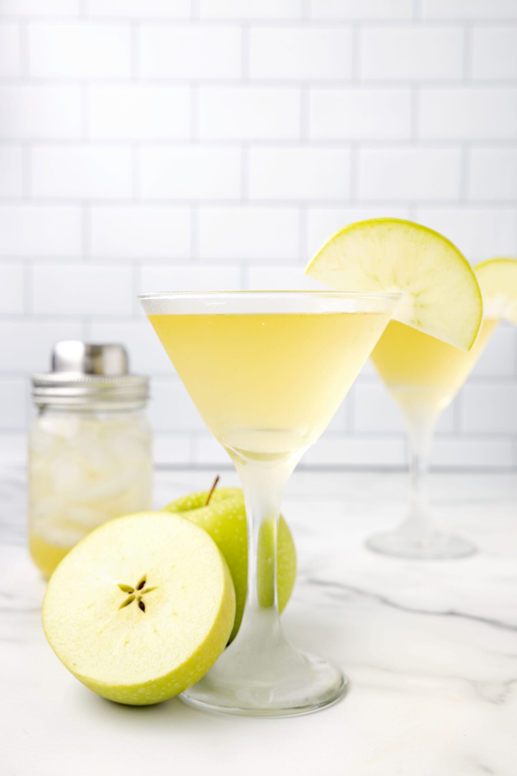Side view of the appletini in a martini glass garnished with a sliced apple.
