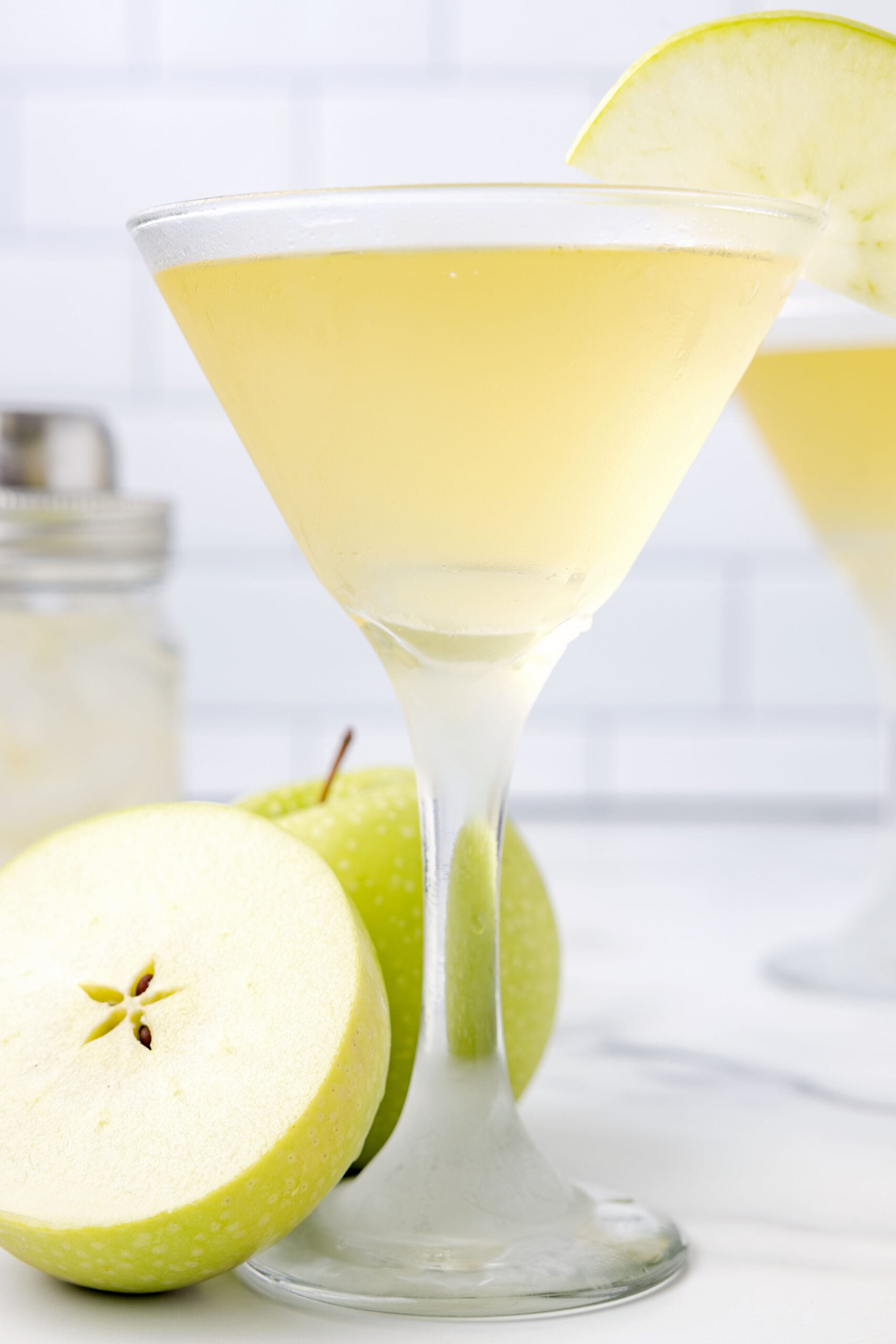 Side view of the appletini in a martini glass garnished with a sliced apple.