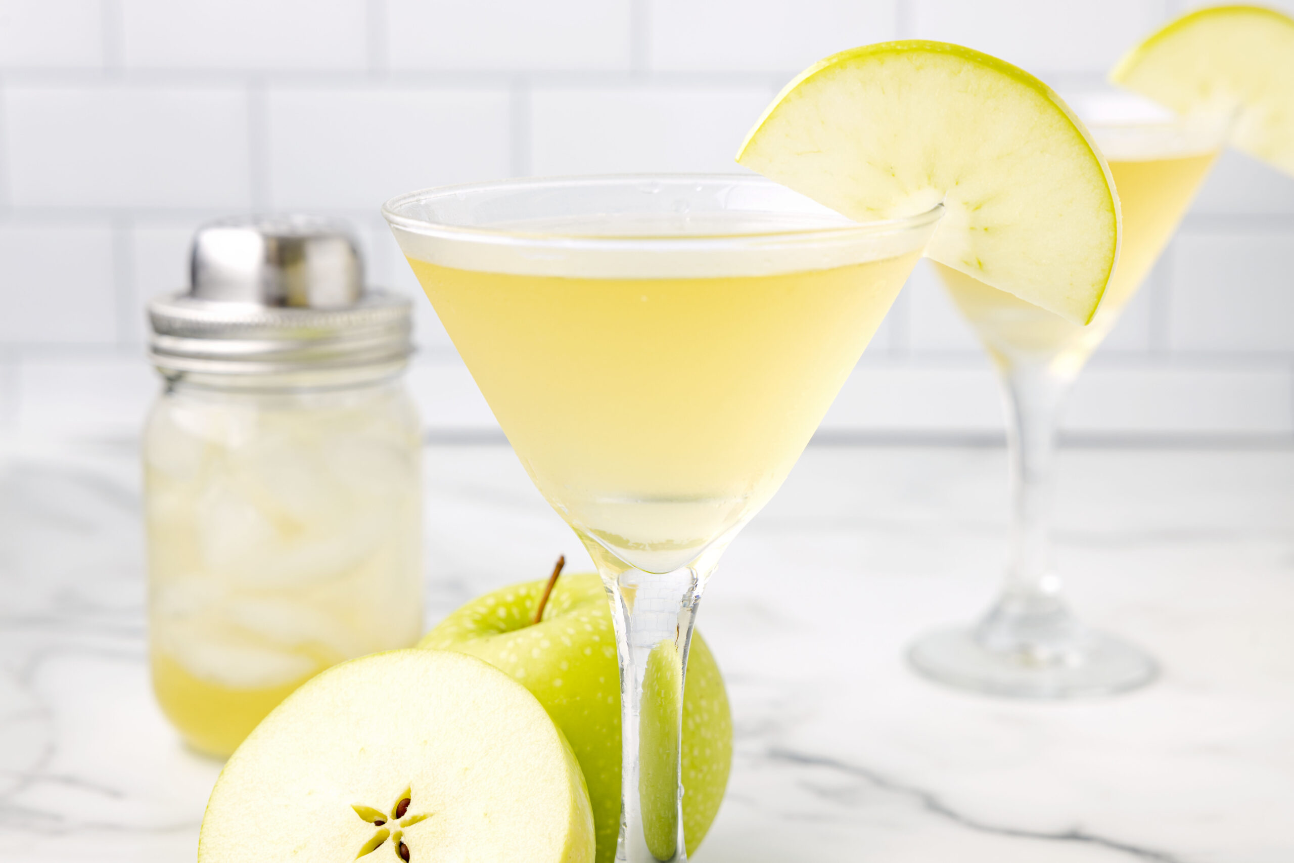 Side view of the appletini in a martini glass garnished with a sliced apple.