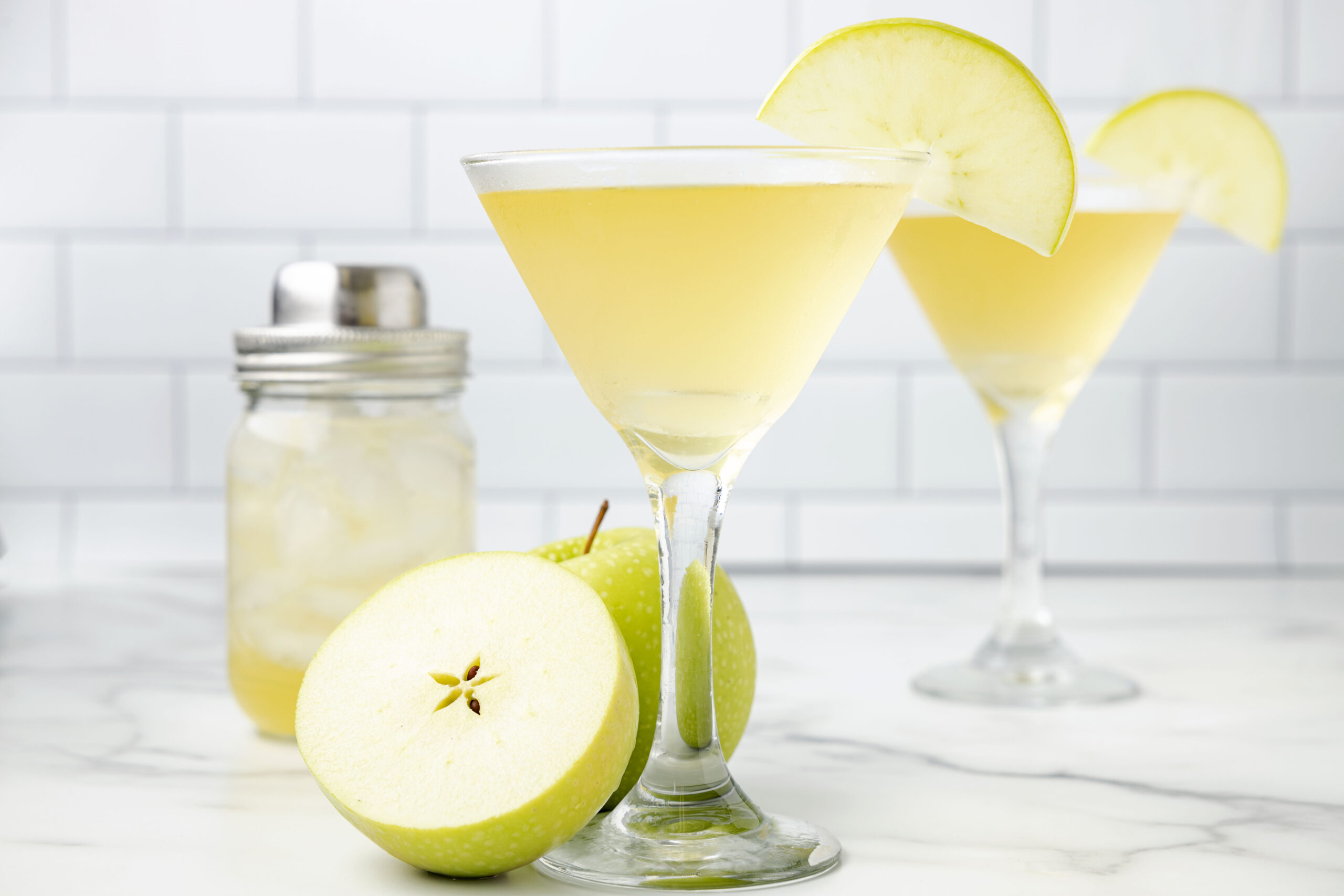 Side view of the appletini in a martini glass garnished with a sliced apple.