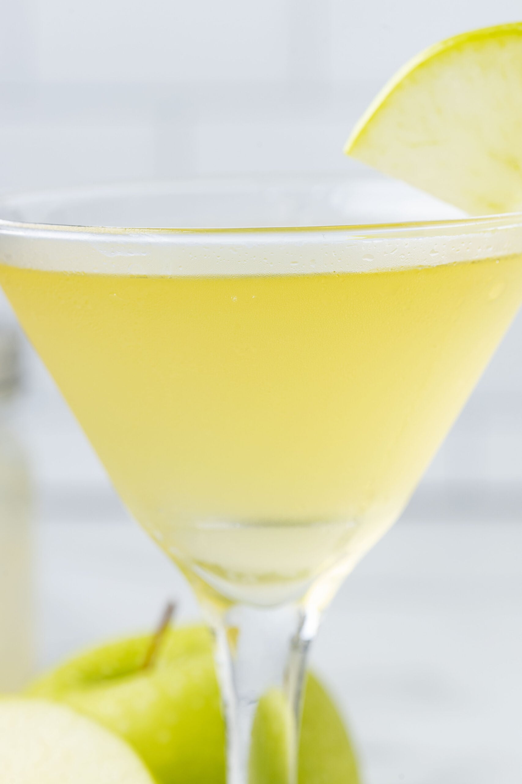 Side view up close of the appletini in a martini glass garnished with a sliced apple.