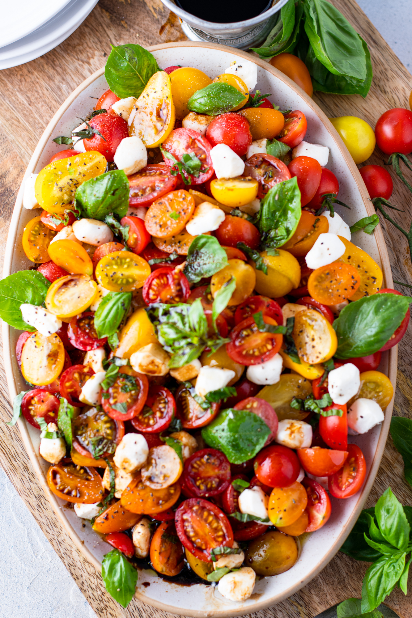 Overhead view of caprese salad on a white oval serving tray. 