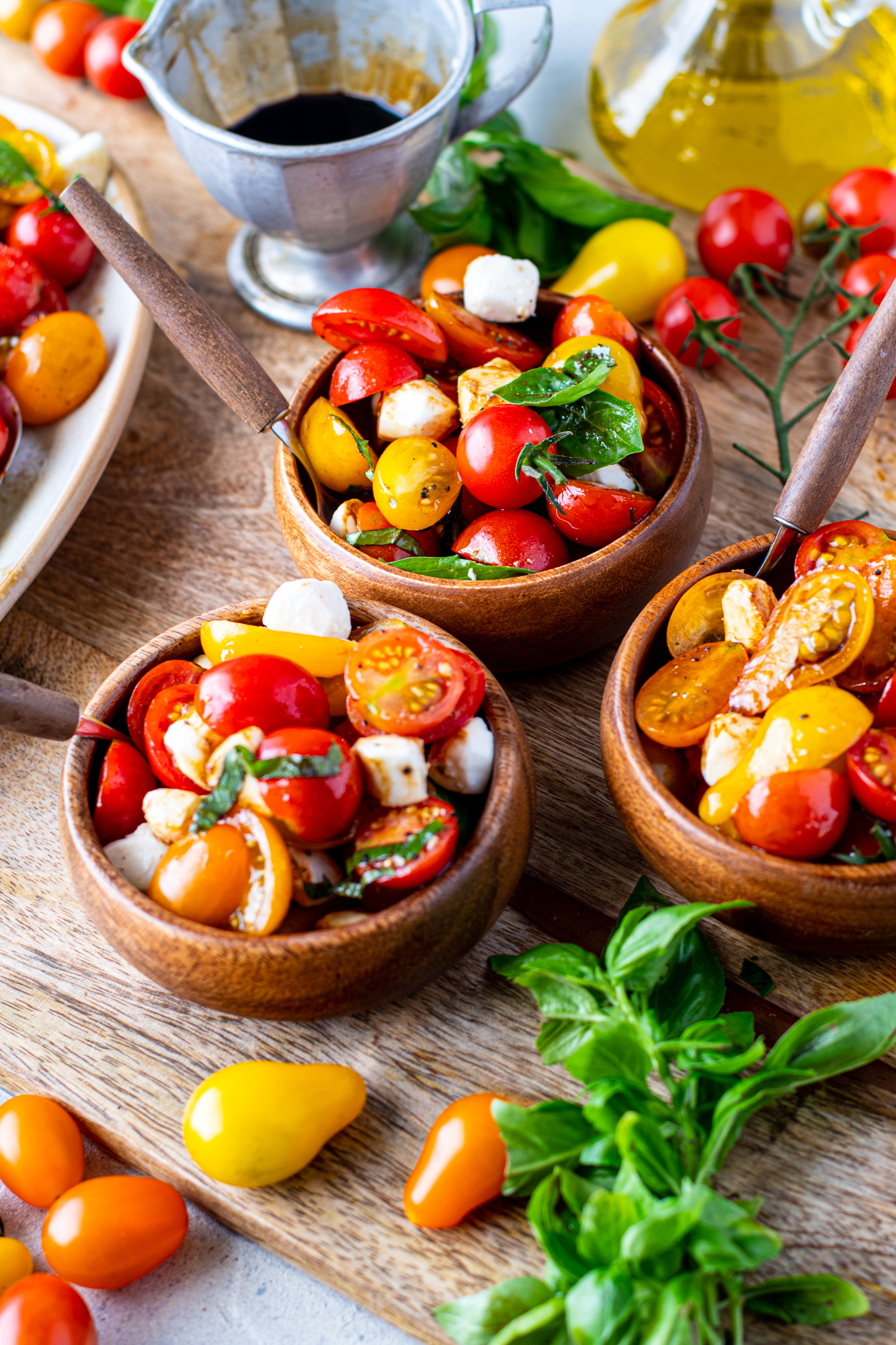Caprese salad in three wooden bowls with silver and wooden forks. 