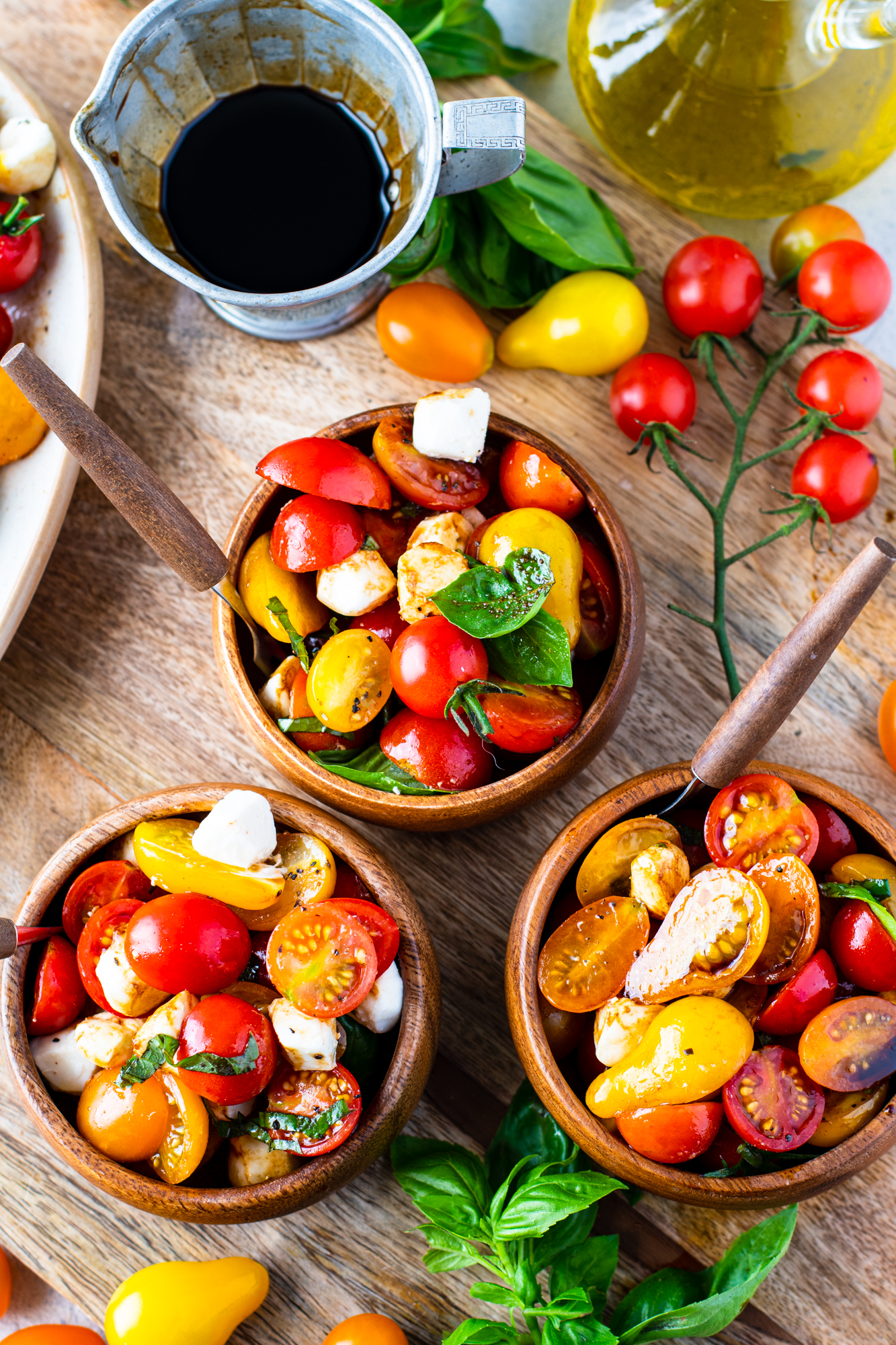 Overhead view of caprese salad in three wooden bowls with silver and wooden forks. 