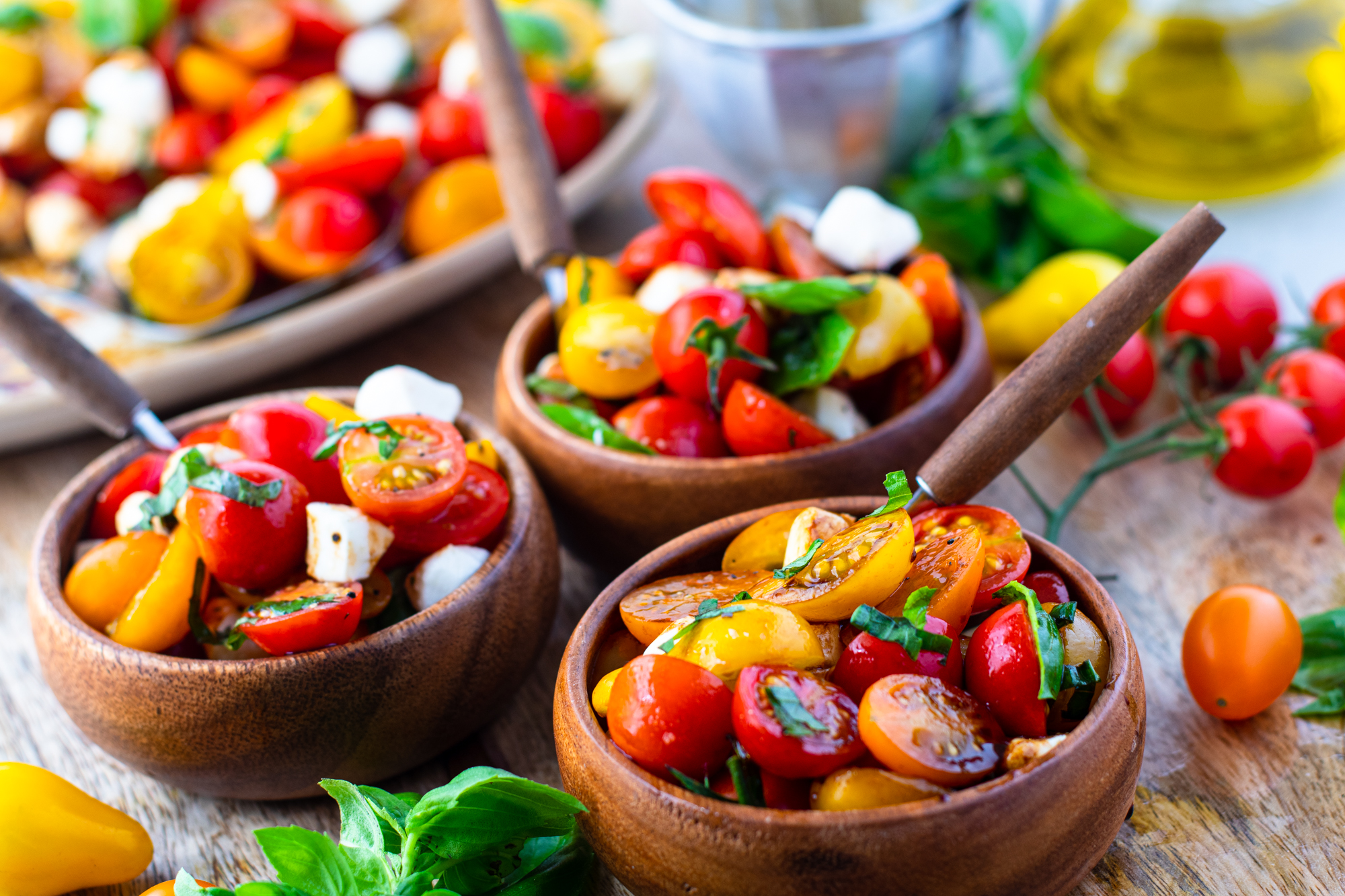 Caprese salad in three wooden bowls with silver and wooden forks. 