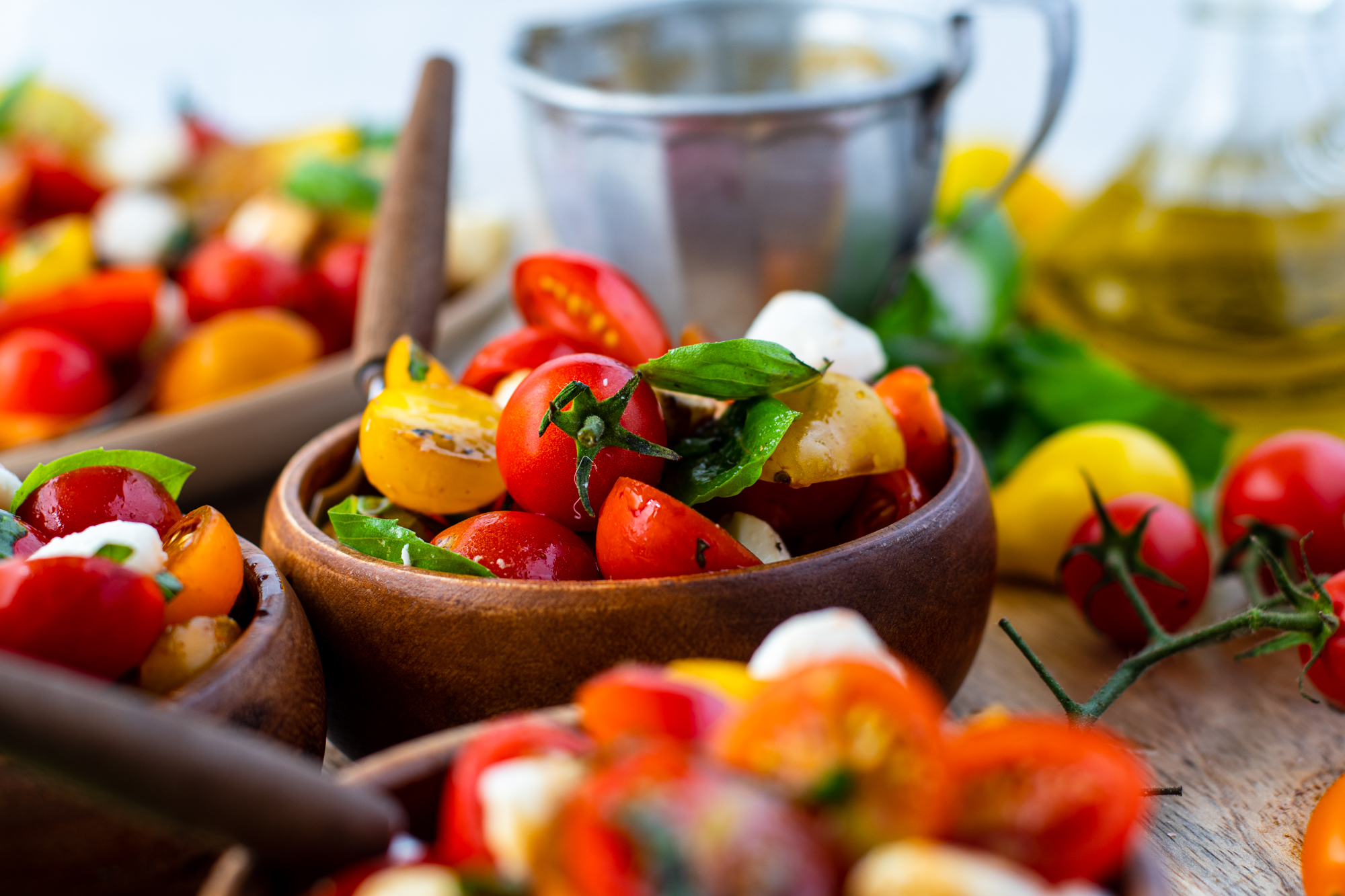 Caprese salad in three wooden bowls with silver and wooden forks. 