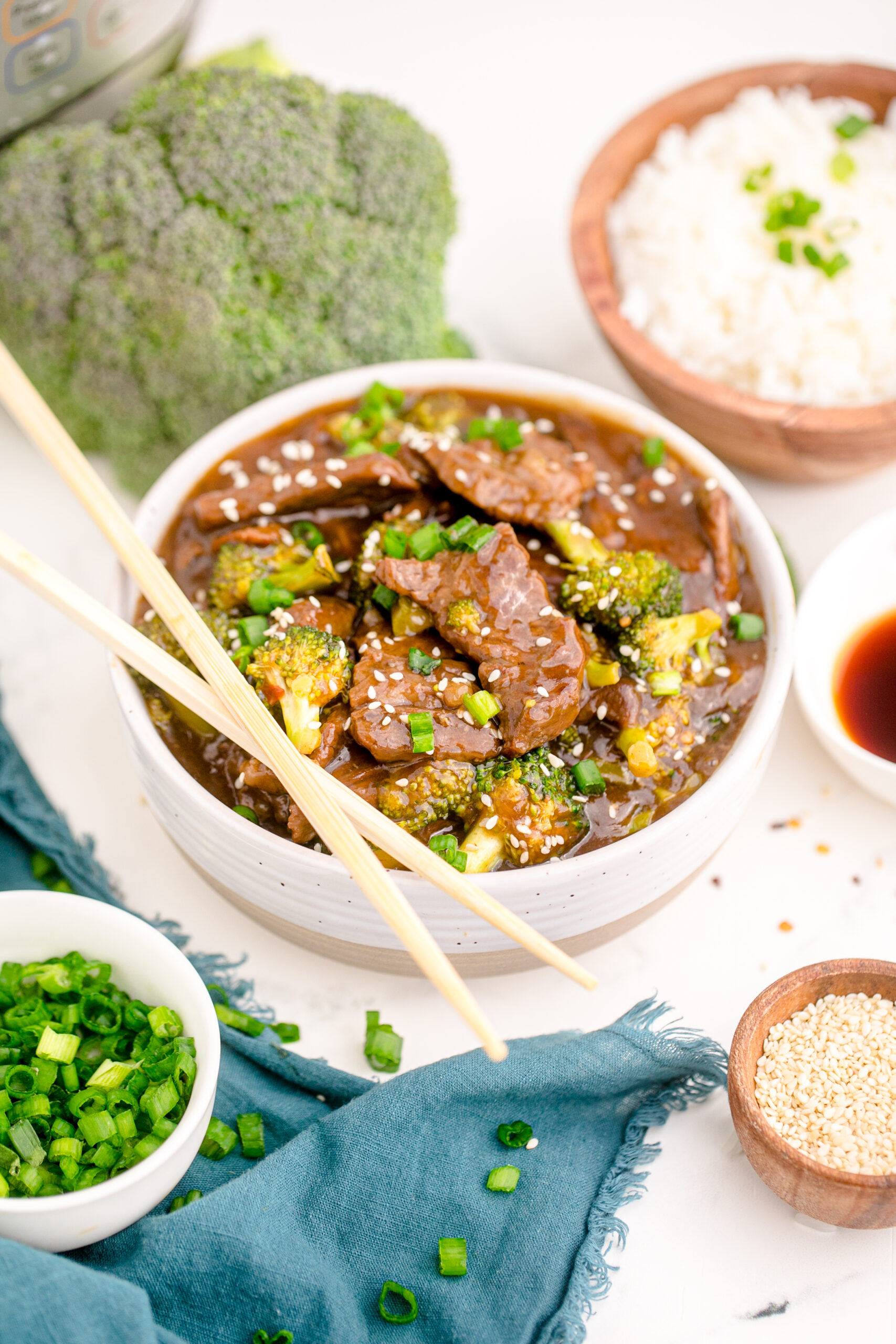 Side view of Instant Pot Beef and Broccoli in a white and tan bowl with a pair of chop sticks balanced on top of bowl.
