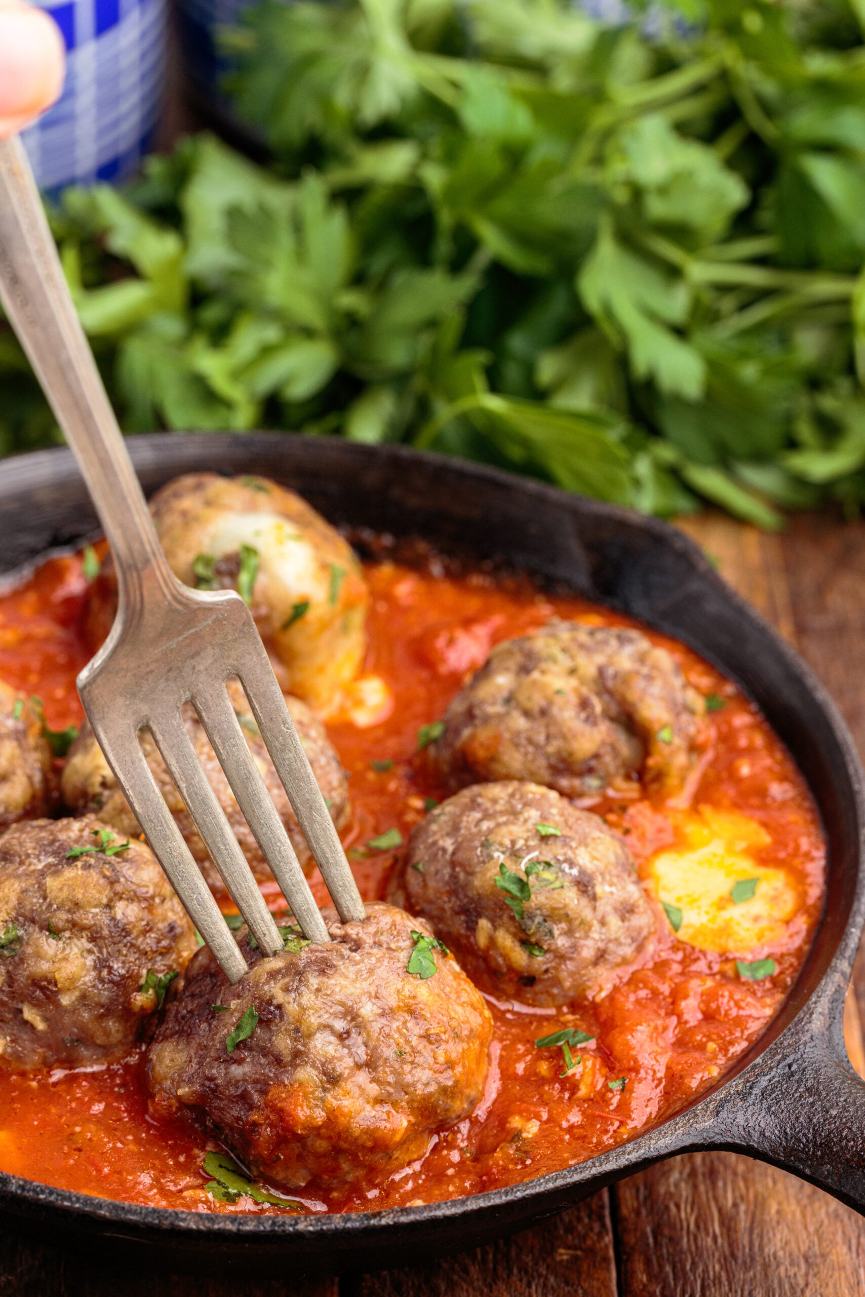 Side view of Mozzarella Stuffed Meatballs in a cast iron skillet with a silver fork impaling a meatball.