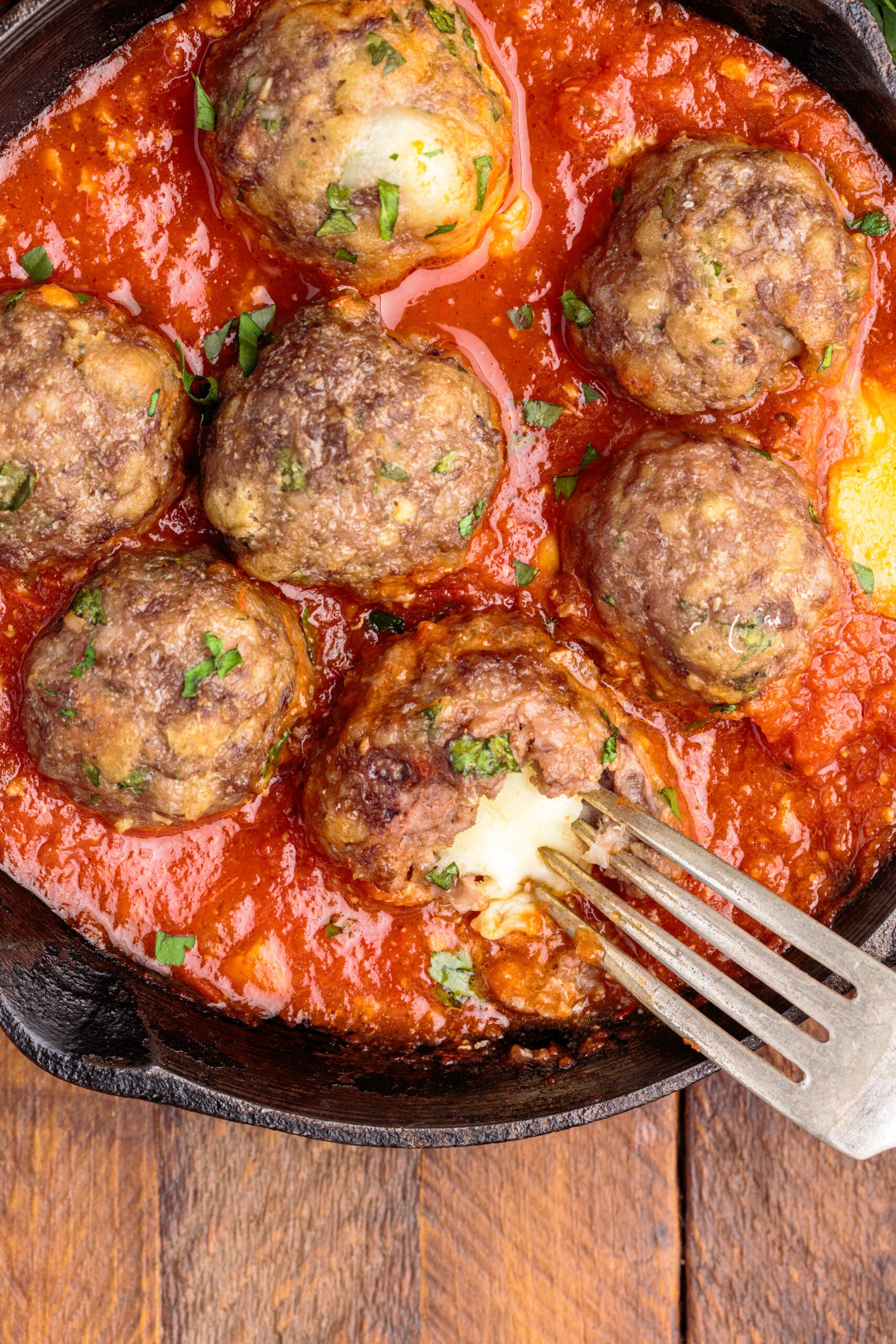 Overhead view of Mozzarella Stuffed Meatballs in a cast iron skillet with one meatball cut open by a silver fork.