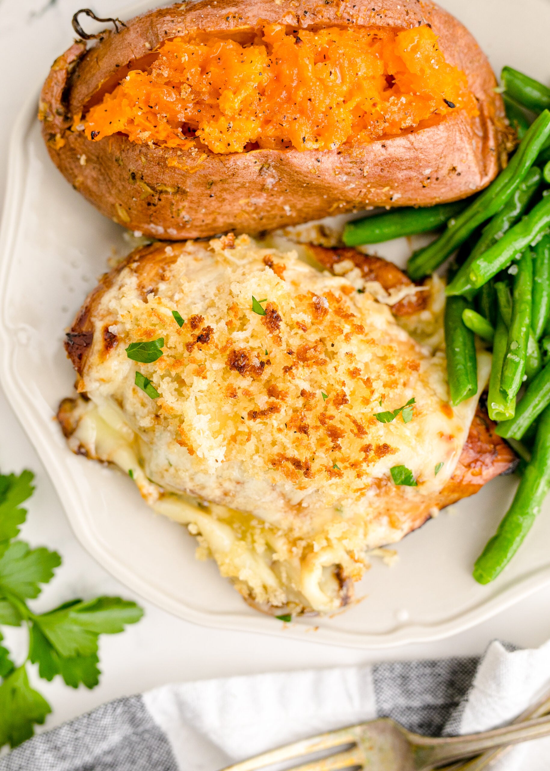 Up close view of Parmesan Crusted Chicken (Longhorn Copycat) on a white dish served with green beans and baked sweet potato.