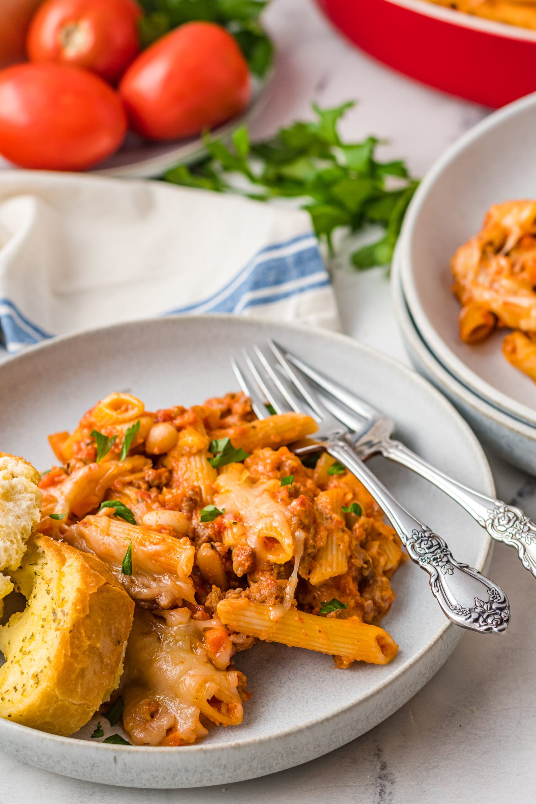 Pasta Fagioli al Forno on a gray dish with a side of garlic bread and two silver forks.
