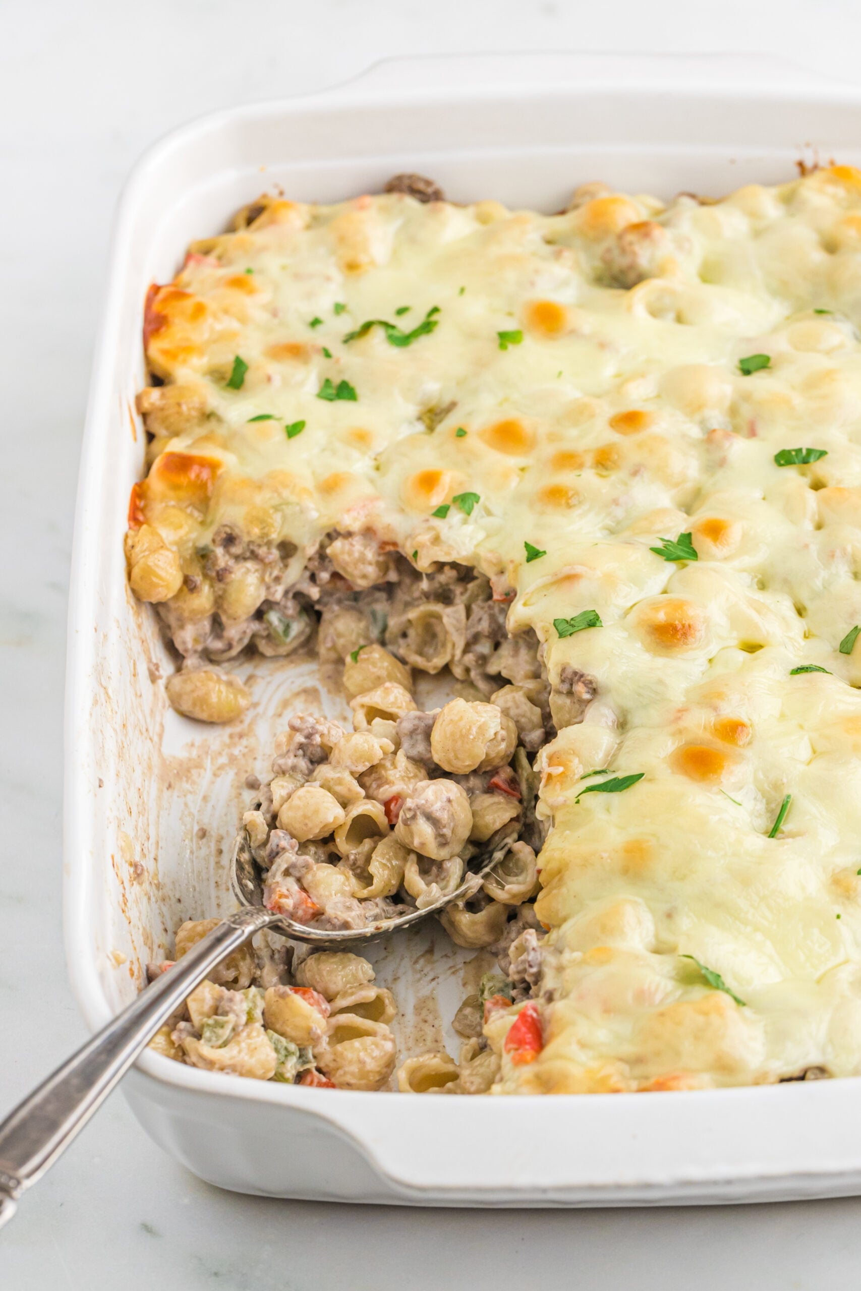 Front view of Philly Cheesesteak Casserole in a white baking dish with a silver spoon.
