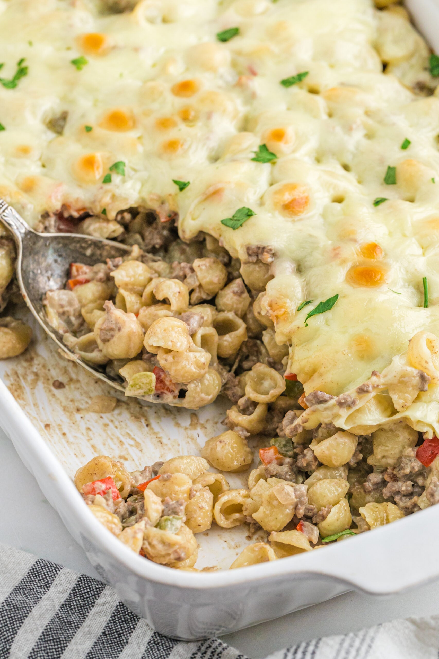 Front view of Philly Cheesesteak Casserole in a white baking dish with a silver spoon.