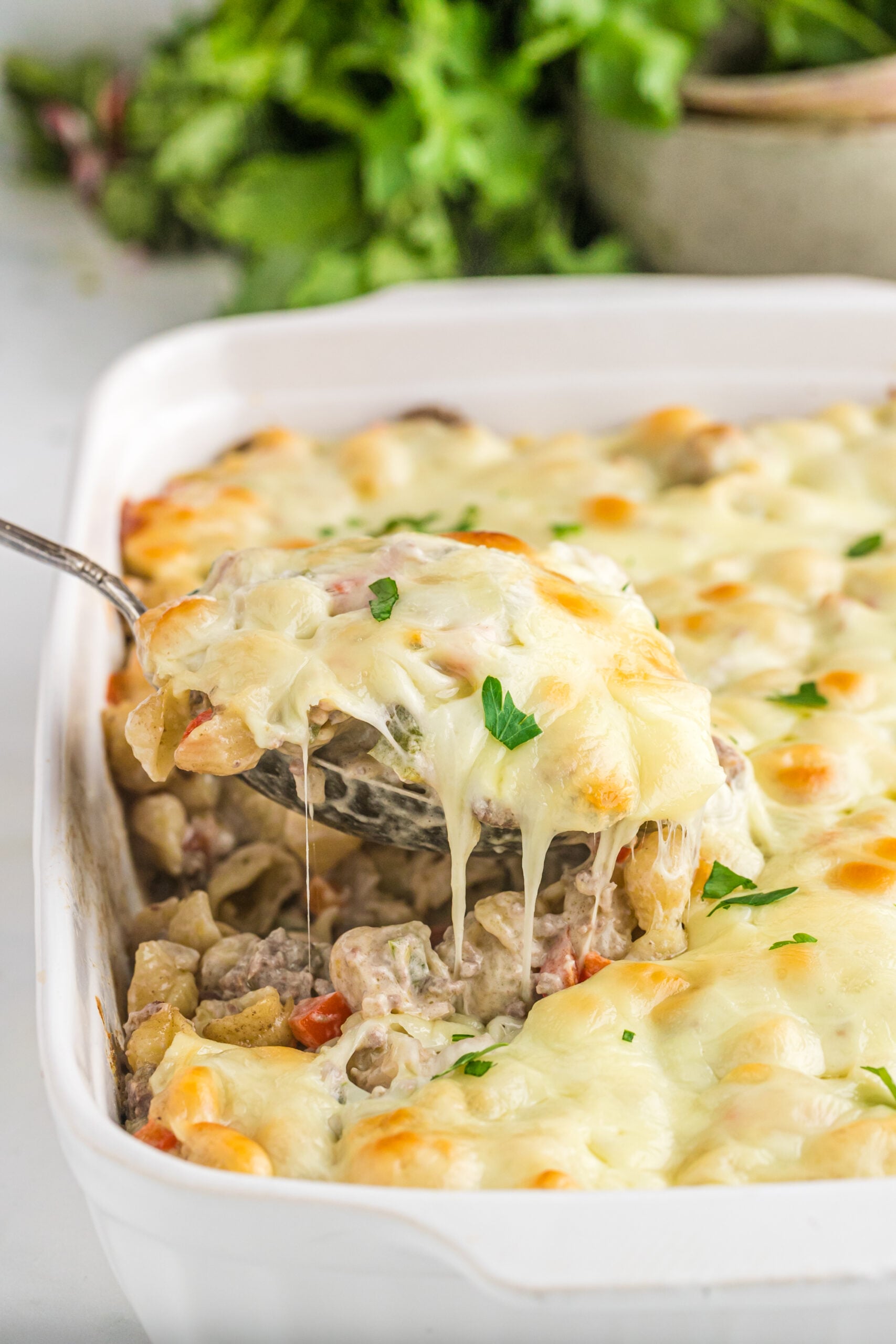 Front view of Philly Cheesesteak Casserole in a white baking dish with a silver spoon removing a spoon full.