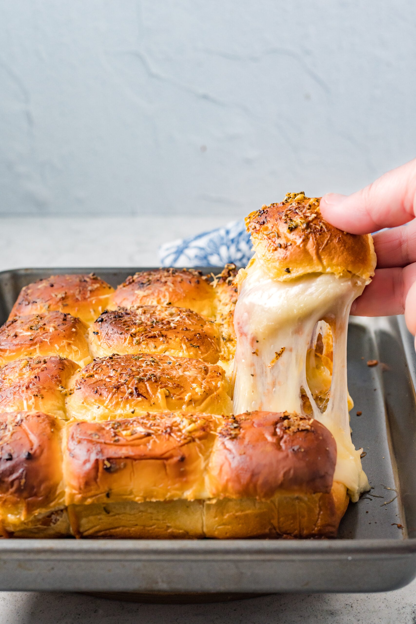 A slider being removed from the baking tray with a gooey cheese pull.