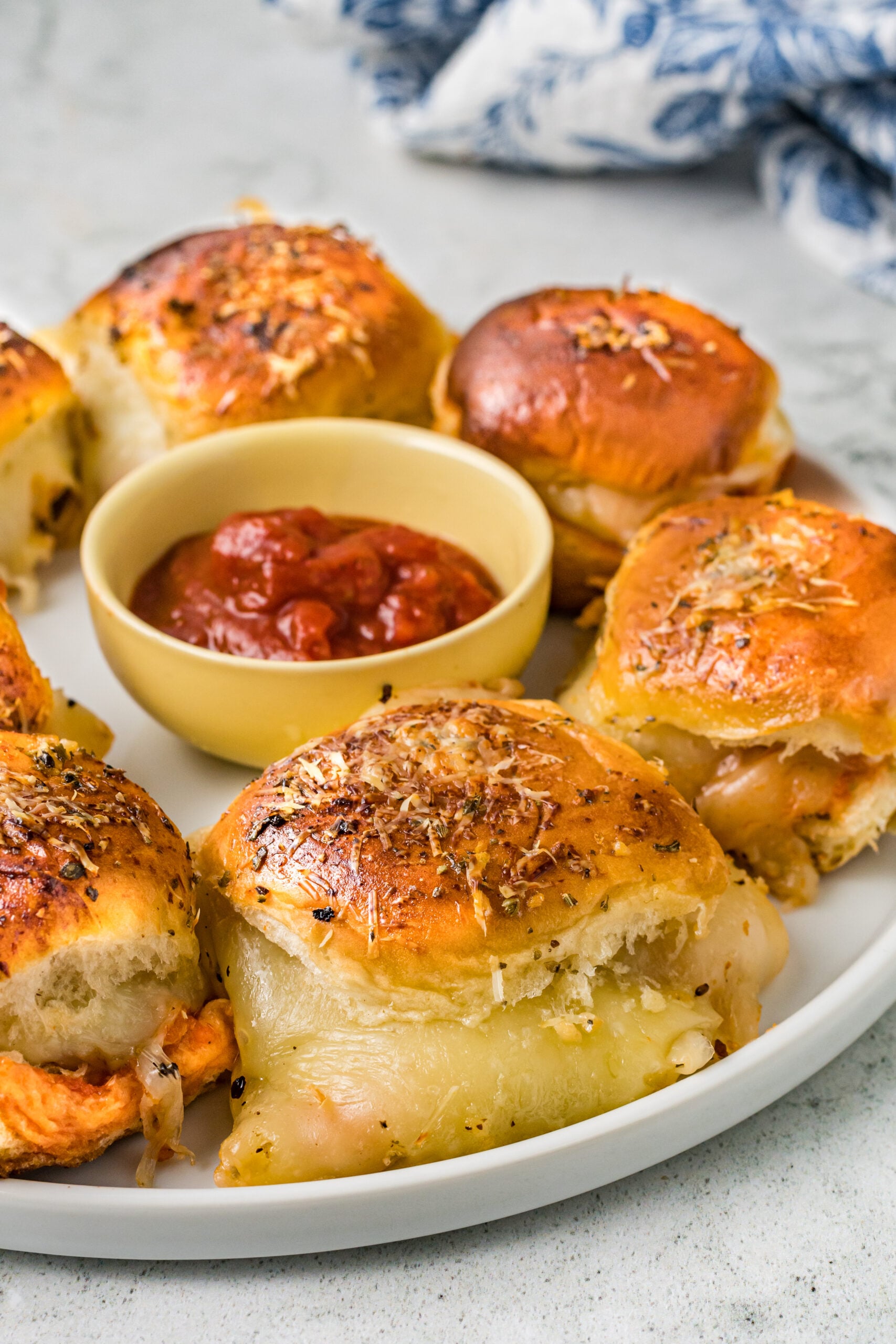 Pizza sliders on a white plate with a bowl of marinara sauce in the center.