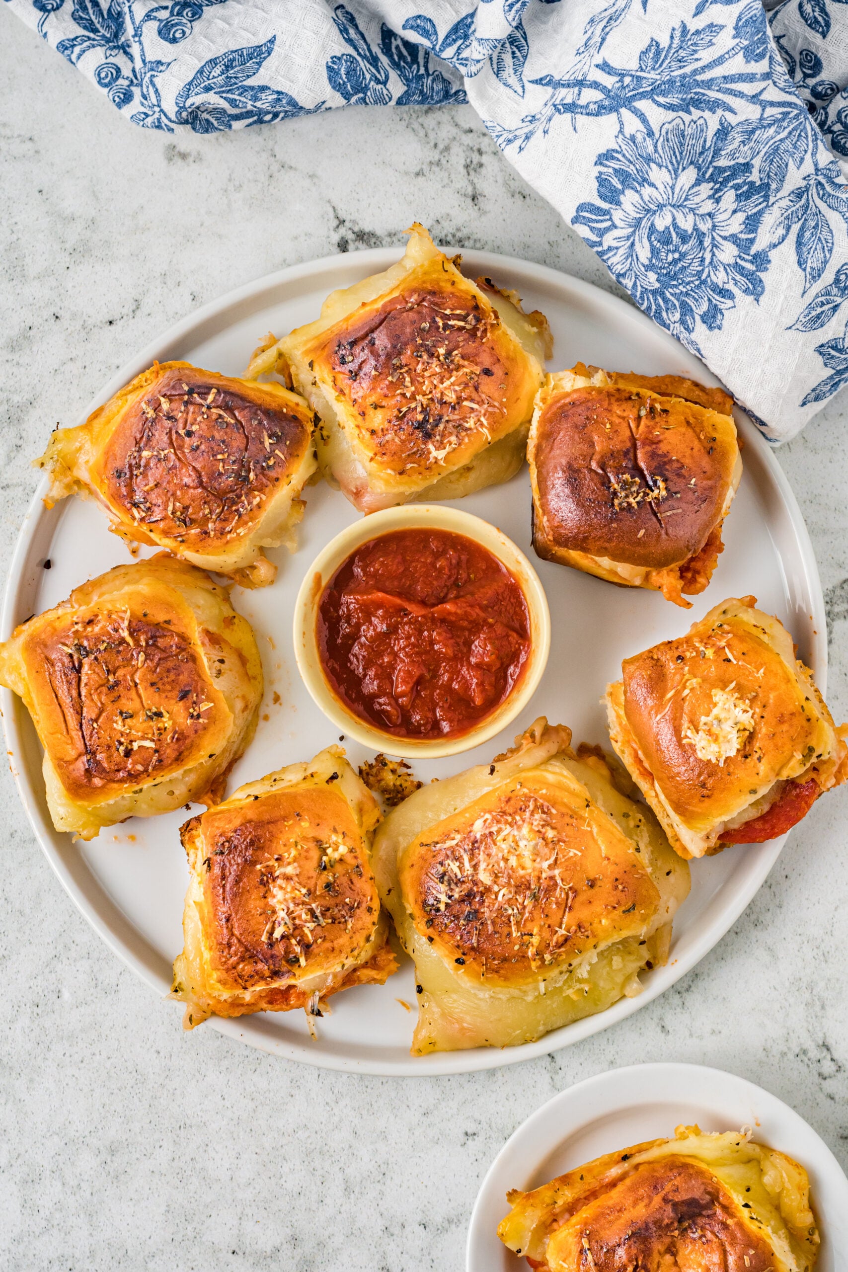 Pizza sliders on a white plate with a bowl of marinara sauce in the center.