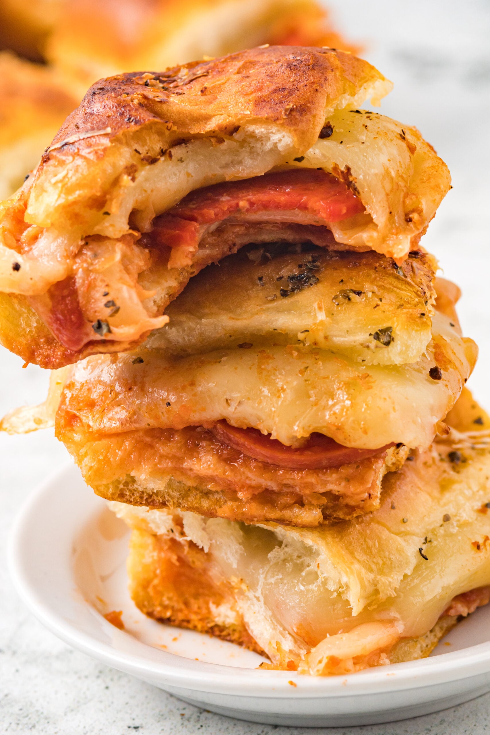 Three pizza sliders stacked on top of each other on a white plate with a bite removed from the top slider.