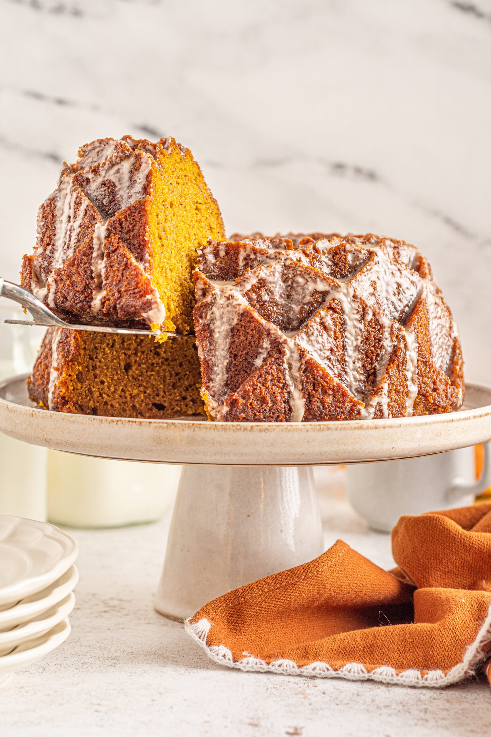 Front view of a slice of Pumpkin Bundt Cake with Cinnamon Sugar Glaze being removed with a silver spatula.