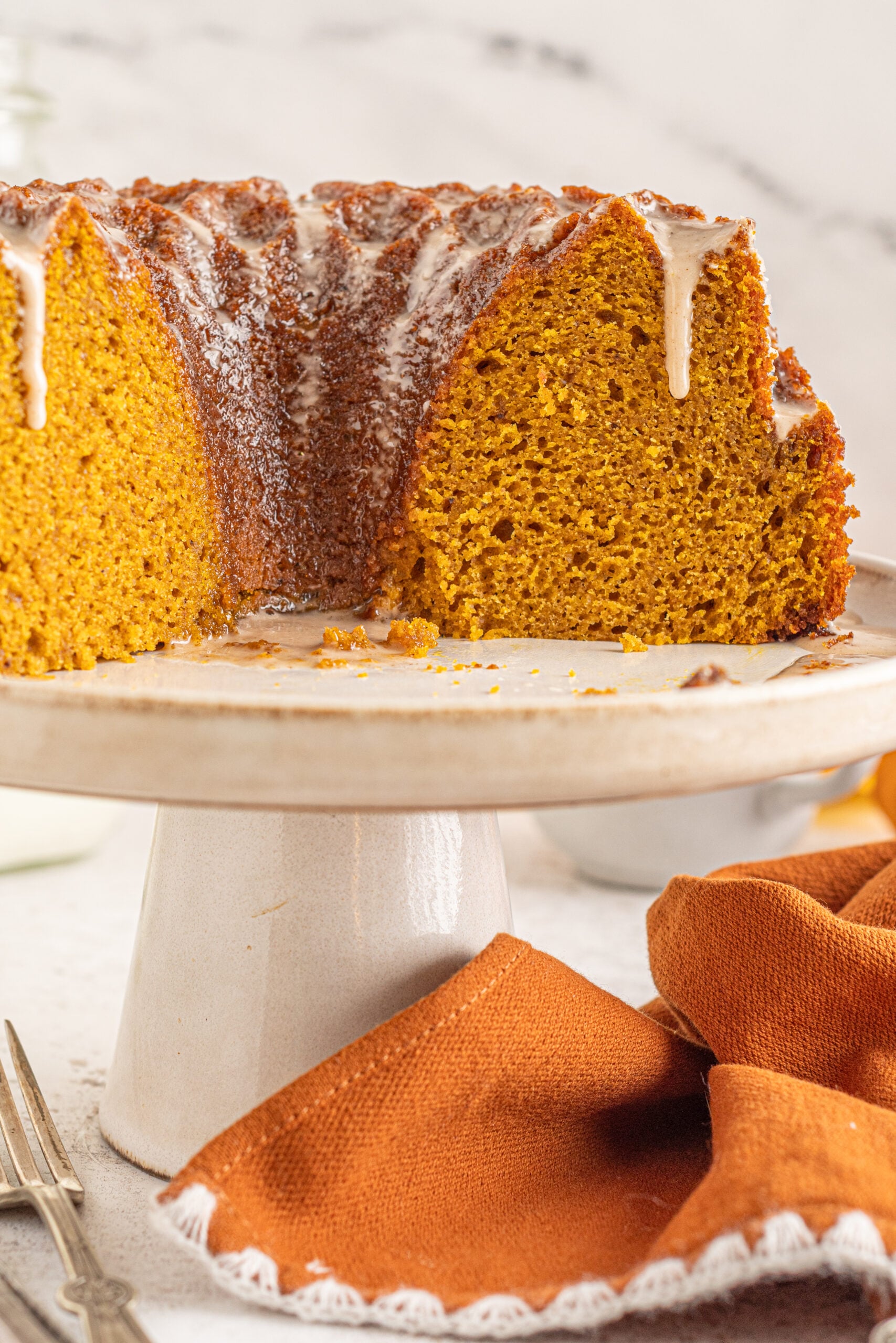 Font view of Pumpkin Bundt Cake with Cinnamon Sugar Glaze with slices removed on a cake stand.