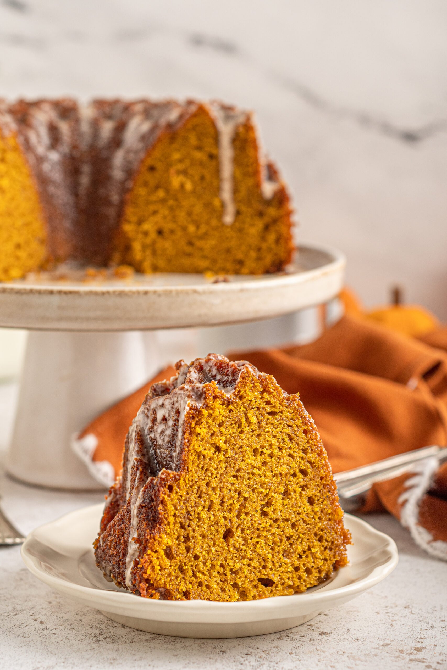 Front view of a slice of Pumpkin Bundt Cake with Cinnamon Sugar Glaze on a white plate.