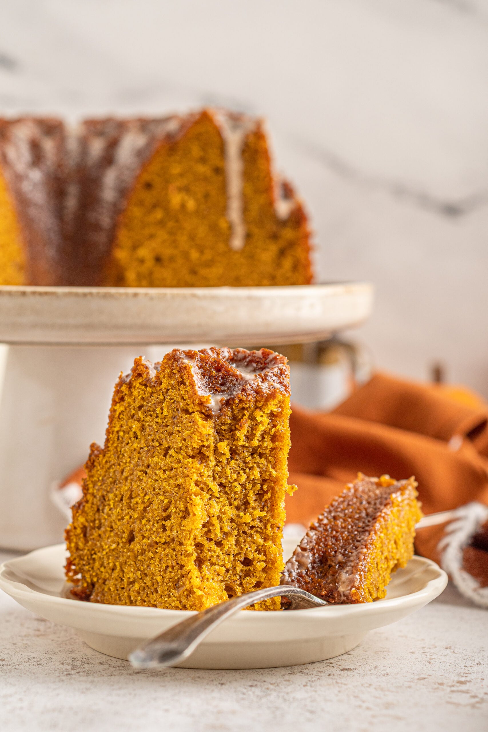 Front view of a slice of Pumpkin Bundt Cake with Cinnamon Sugar Glaze with a bite removed by a silver fork.