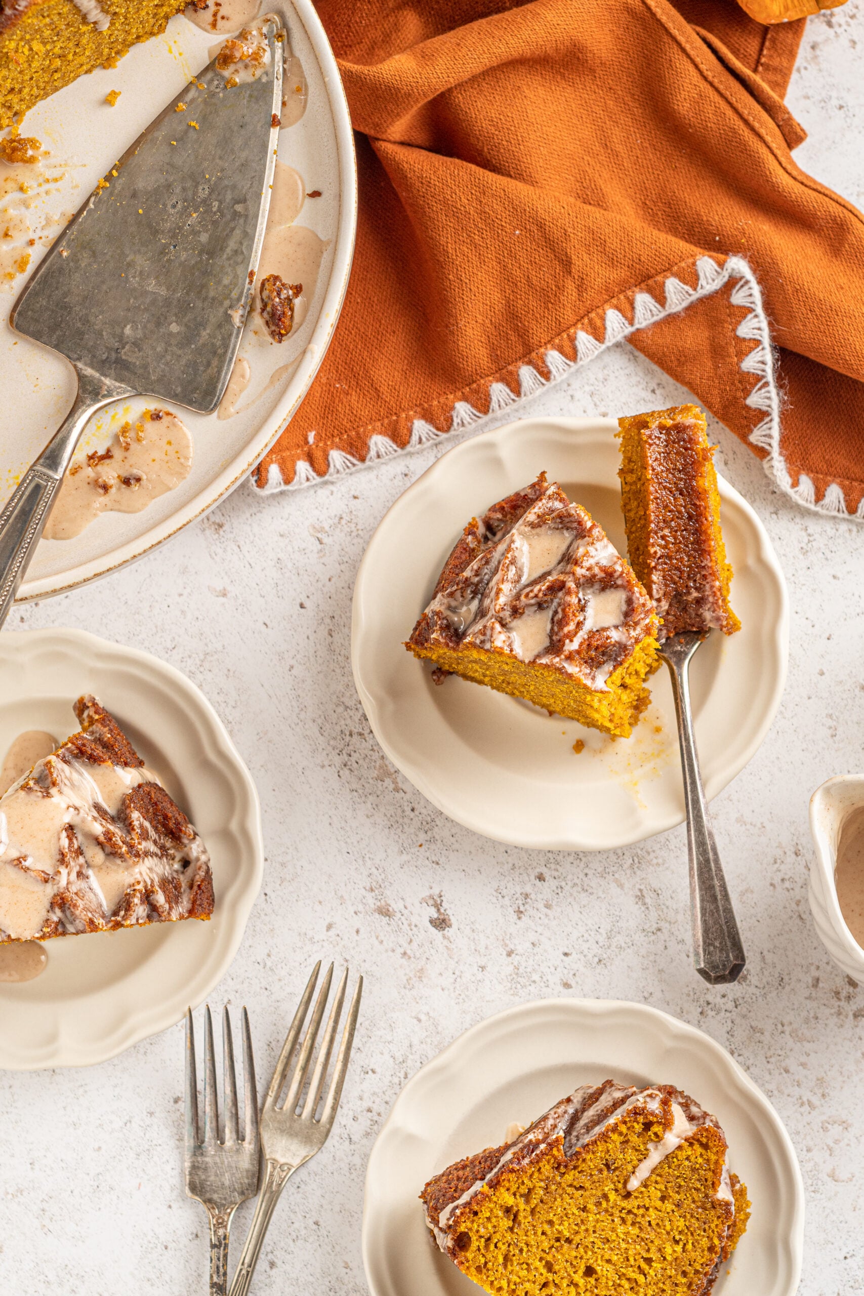 Slices of Pumpkin Bundt Cake with Cinnamon Sugar Glaze on white dishes with a bite removed by a silver fork.