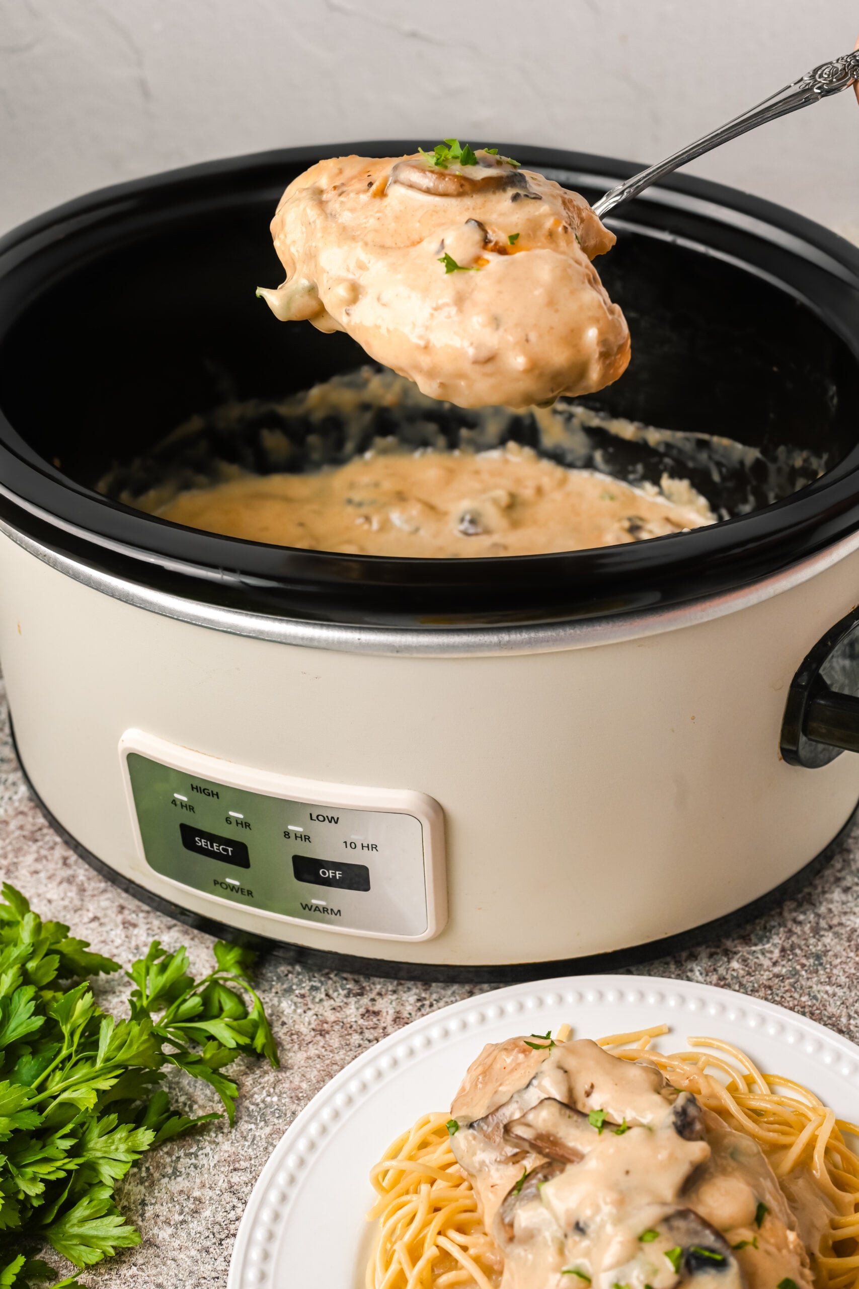 Image of the marsala chicken being removed from the slow cooker and plated on top of spaghetti noodles.