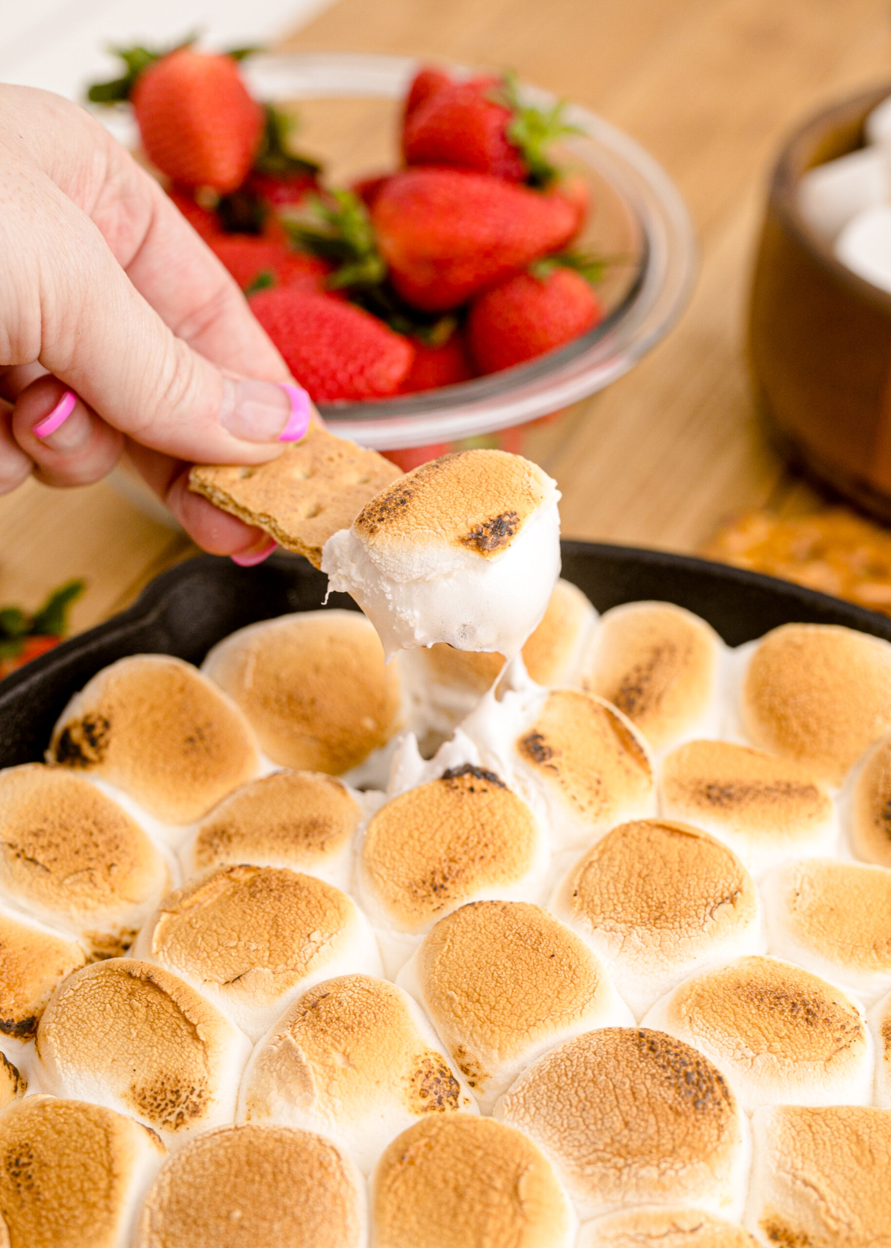 Close up view of S'mores dip in a cast iron skillet with a graham cracker dipped in the dip.