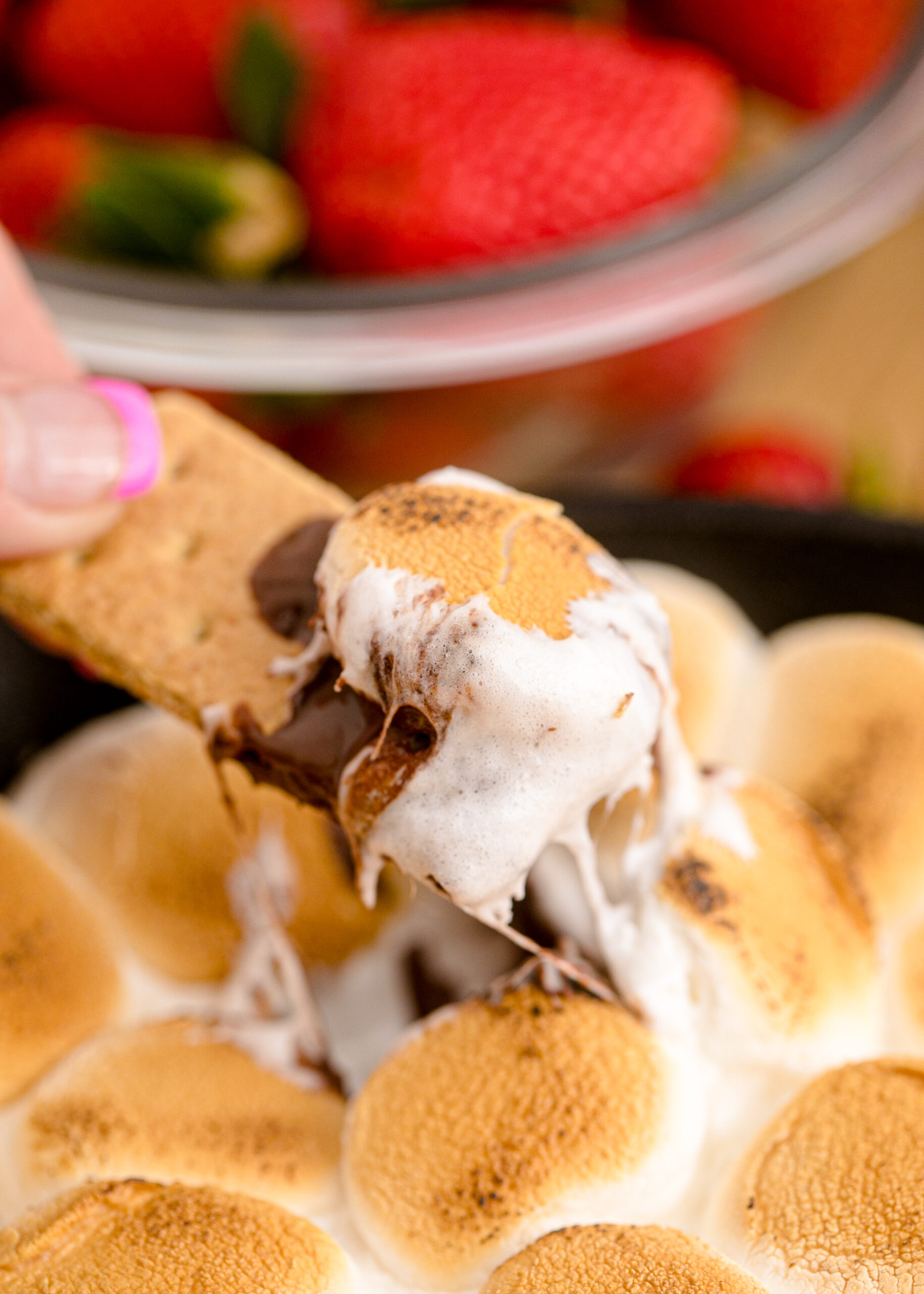Close up view of S'mores dip in a cast iron skillet with a graham cracker dipped in the dip.