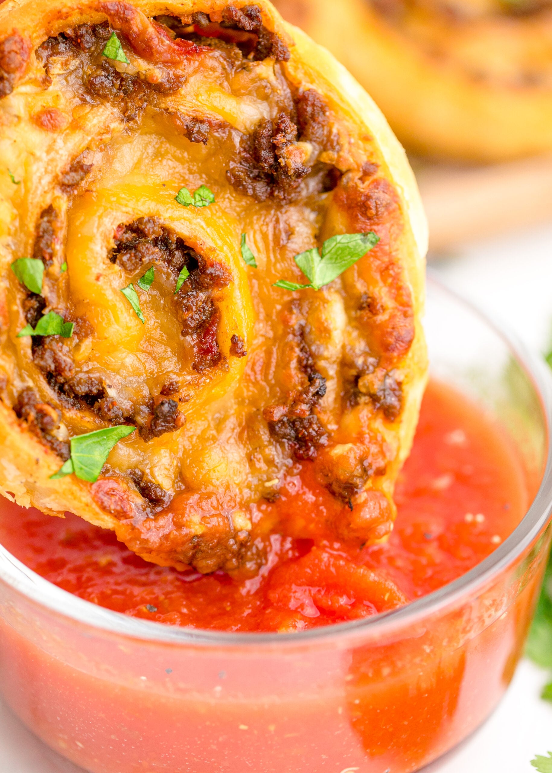 Up close view of Taco Pinwheel being dipped into a clear bowl filled with salsa.