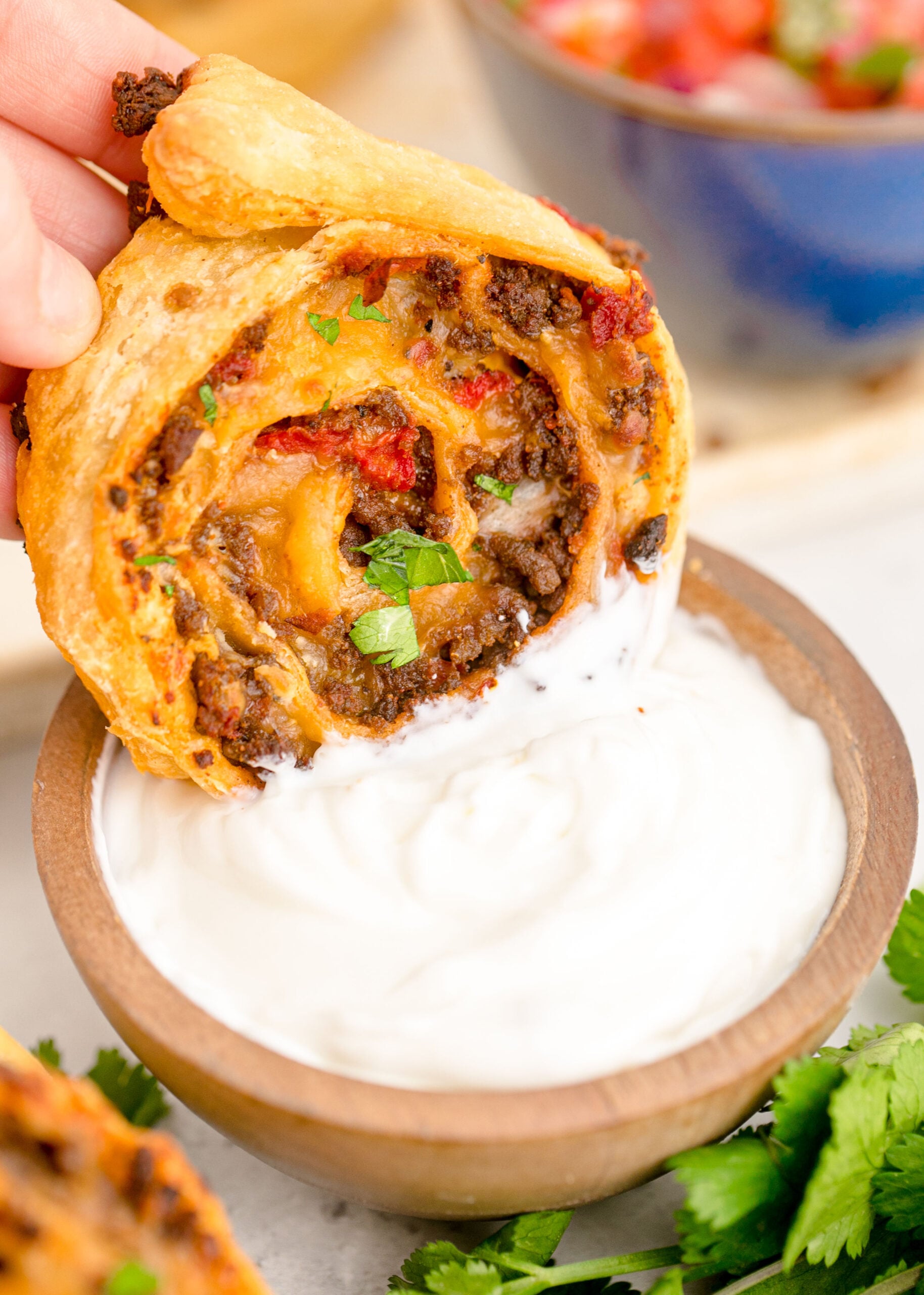 Up close view of Taco Pinwheel being dipped into a wooden bowl filled with ranch dressing.