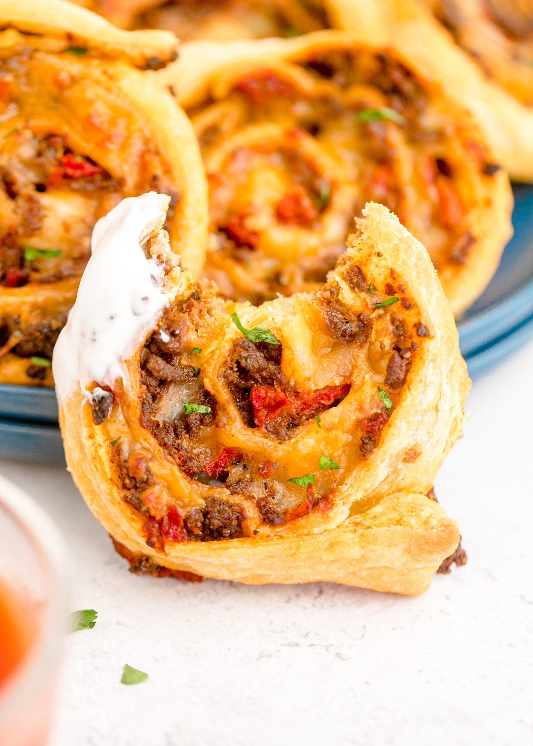 Up close view of a propped up Taco Pinwheel with ranch dressing and a bite removed.