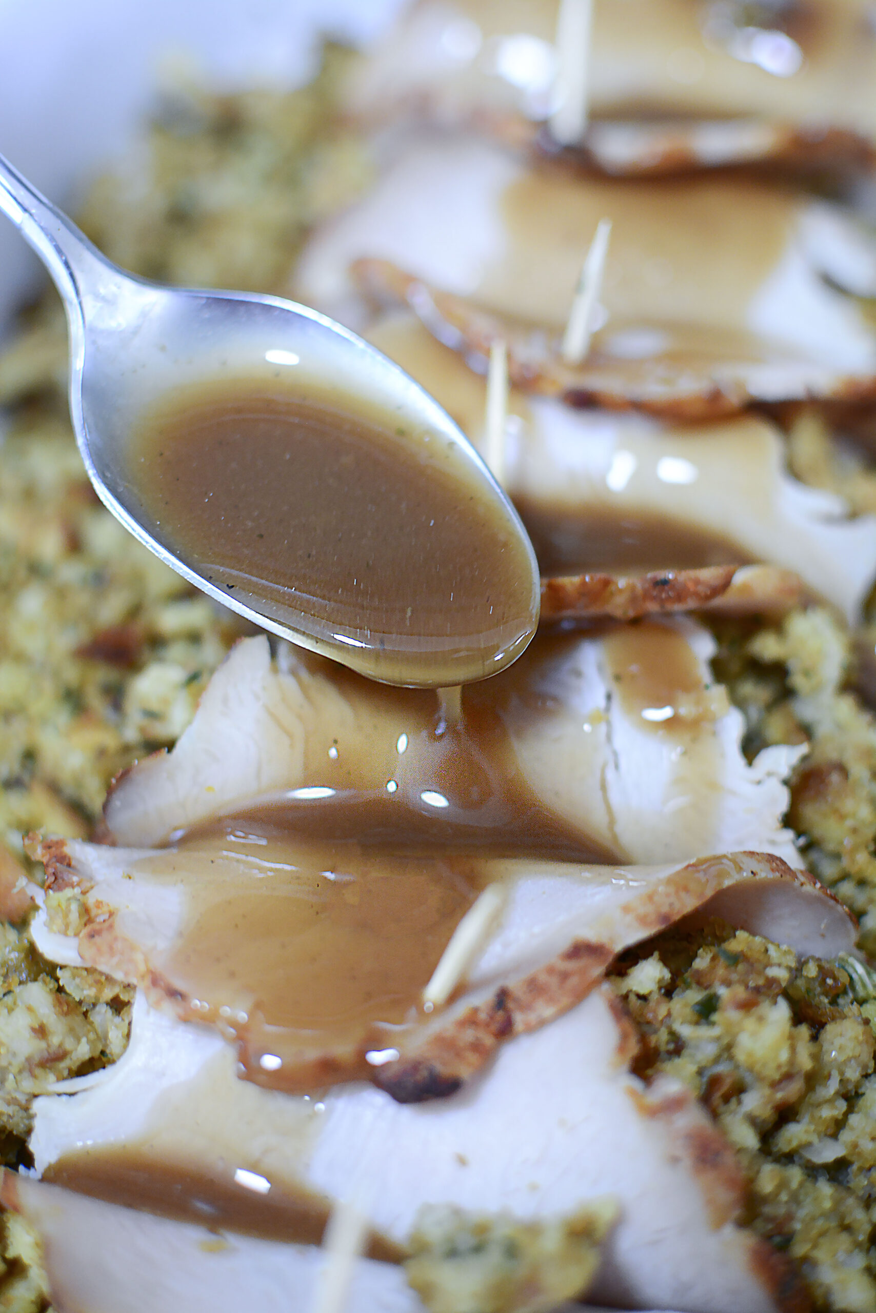  A silver spoon spooning gravy over turkey stuffing rolls. 