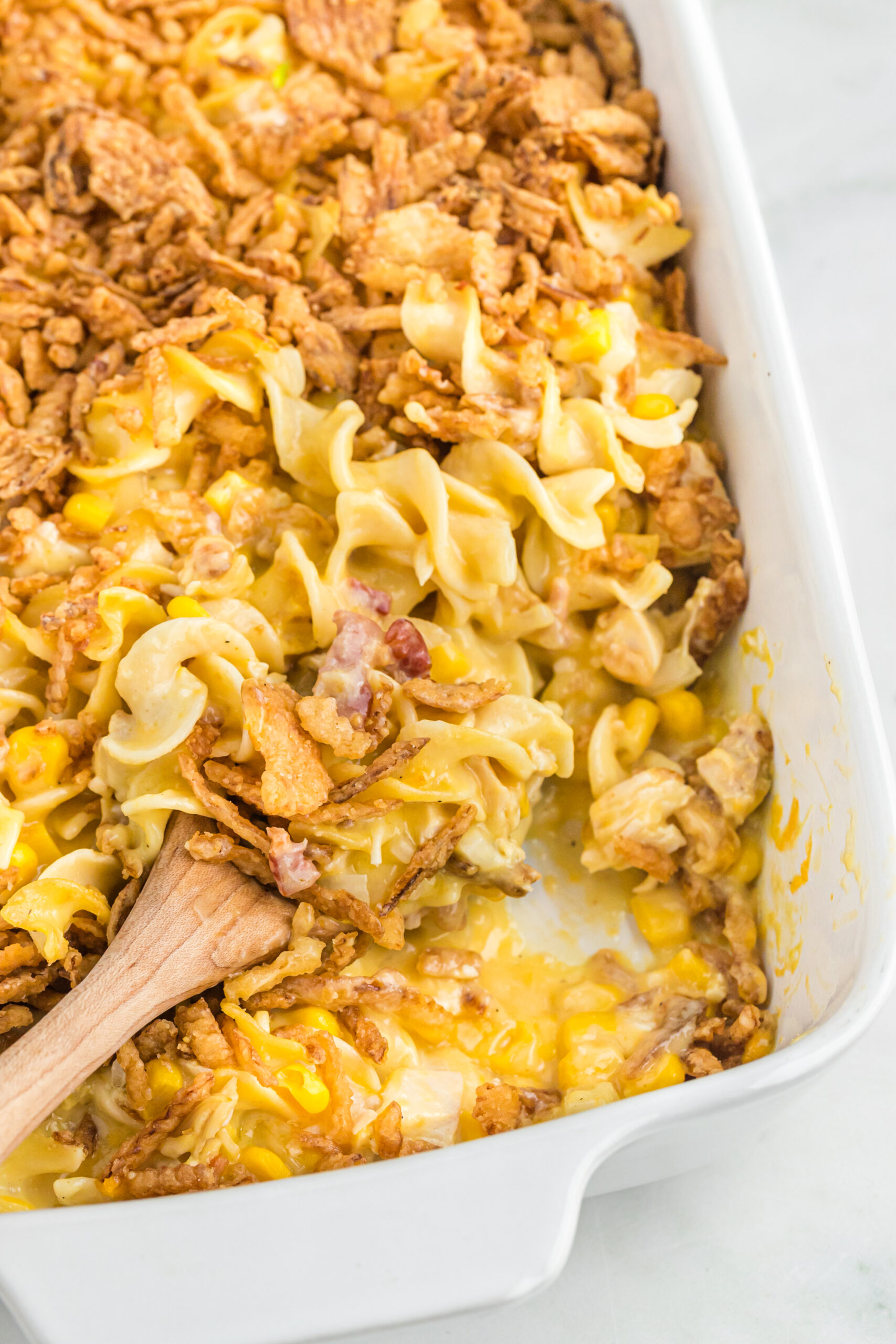 Overhead view of Ultimate Chicken Casserole in a white baking dish with a wooden spoon removing a portion.