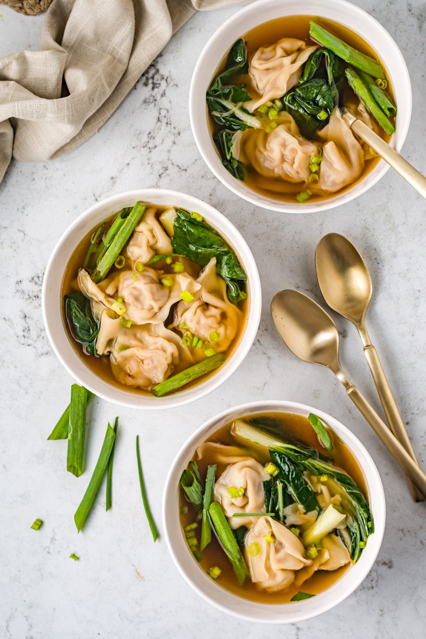 Overhead view of Wonton Soup in three white bowls topped with sliced green onion.
