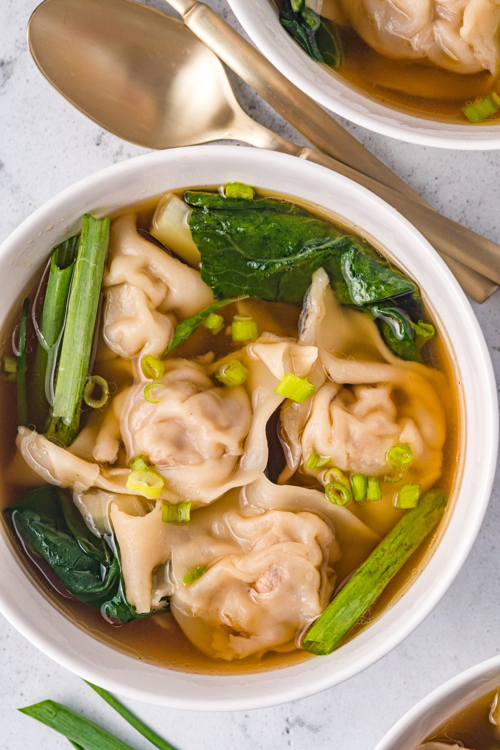 Overhead view of Wonton Soup in a white bowl topped with sliced green onion.