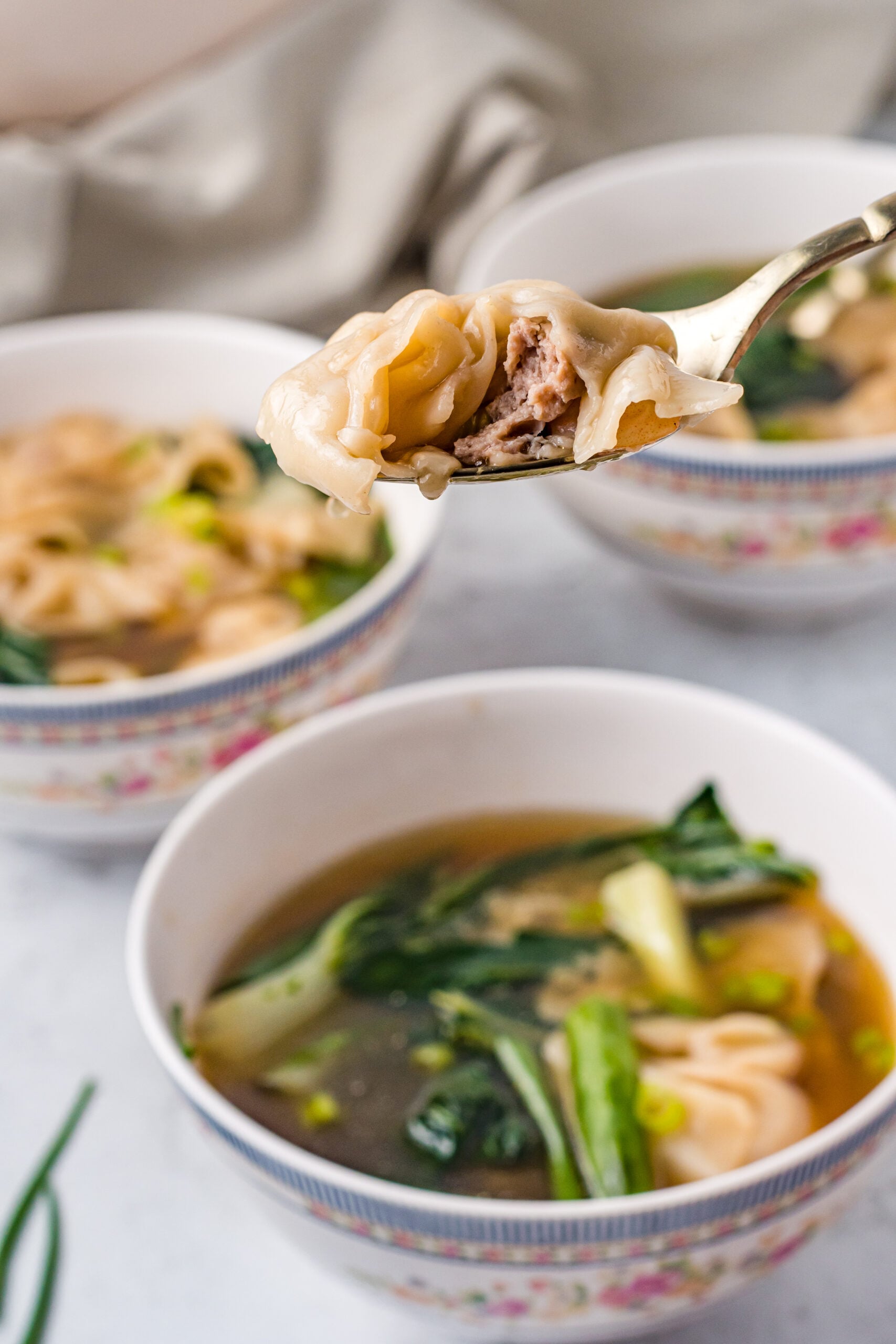 A gold spoon holding up wonton soup.