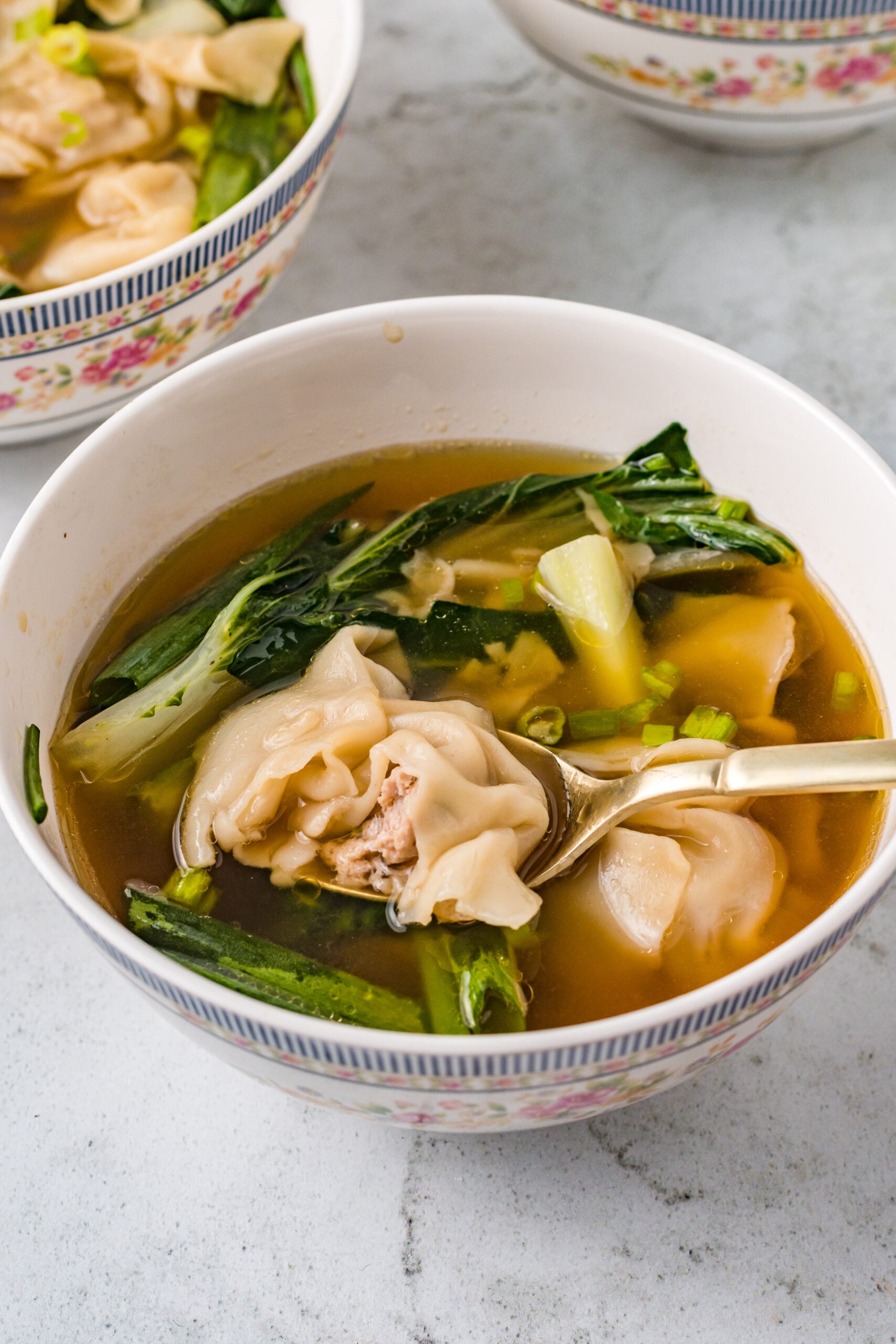 Wonton Soup in a white bowl with a gold spoon removing a bite.